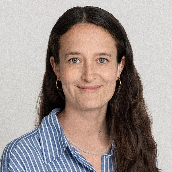 Laura Warnecke, Psychologische Psychotherapeutin, blickt freundlich zugewandt, lange braune Haare, trägt Ohrringe und blau weiß gestreiftes Hemd.