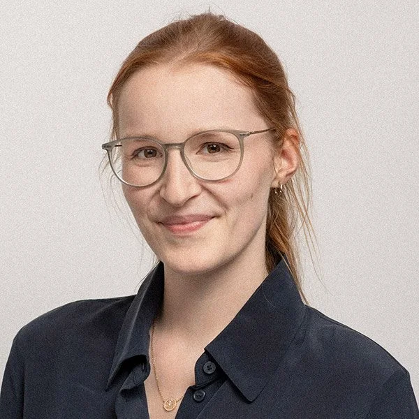 Caroline Lanta, Psychologische Psychotherapeutin, freundlich blickend, rotes Haar im Pferdeschwanz, trägt Brille und blaues Hemd.