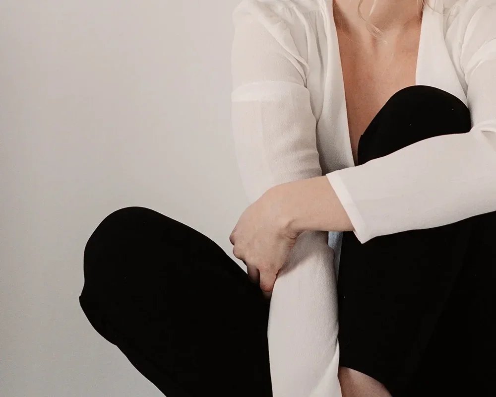 Frau in professioneller Kleidung sitzt nachdenklich auf dem Boden, überlegt und fokussiert