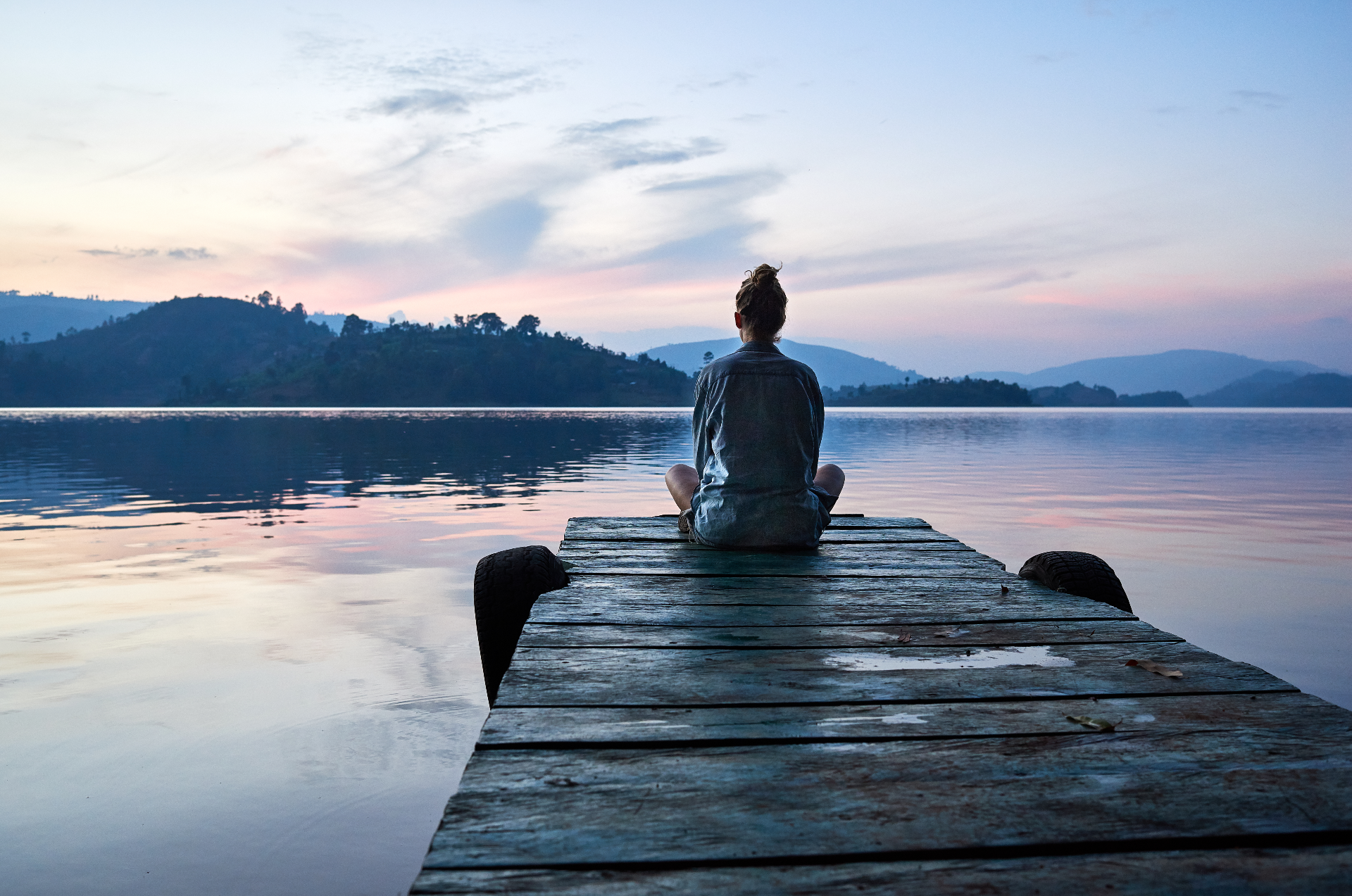 Person sitting peacefully on a jetty at dusk overlooking a calm lake, representing reflection and emotional wellbeing