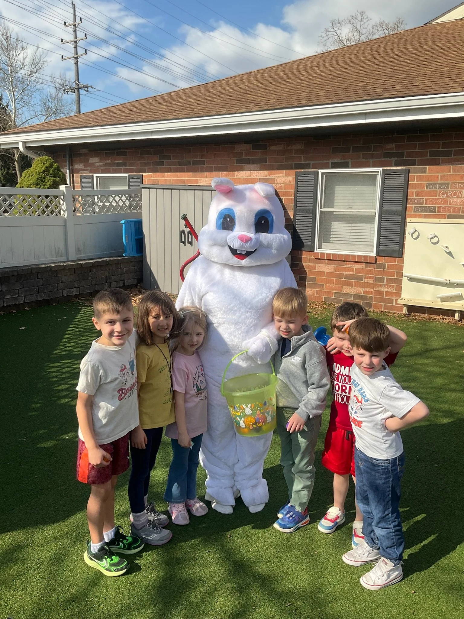 Children gathered outdoors with a person in a bunny costume holding an Easter basket during a daytime event.