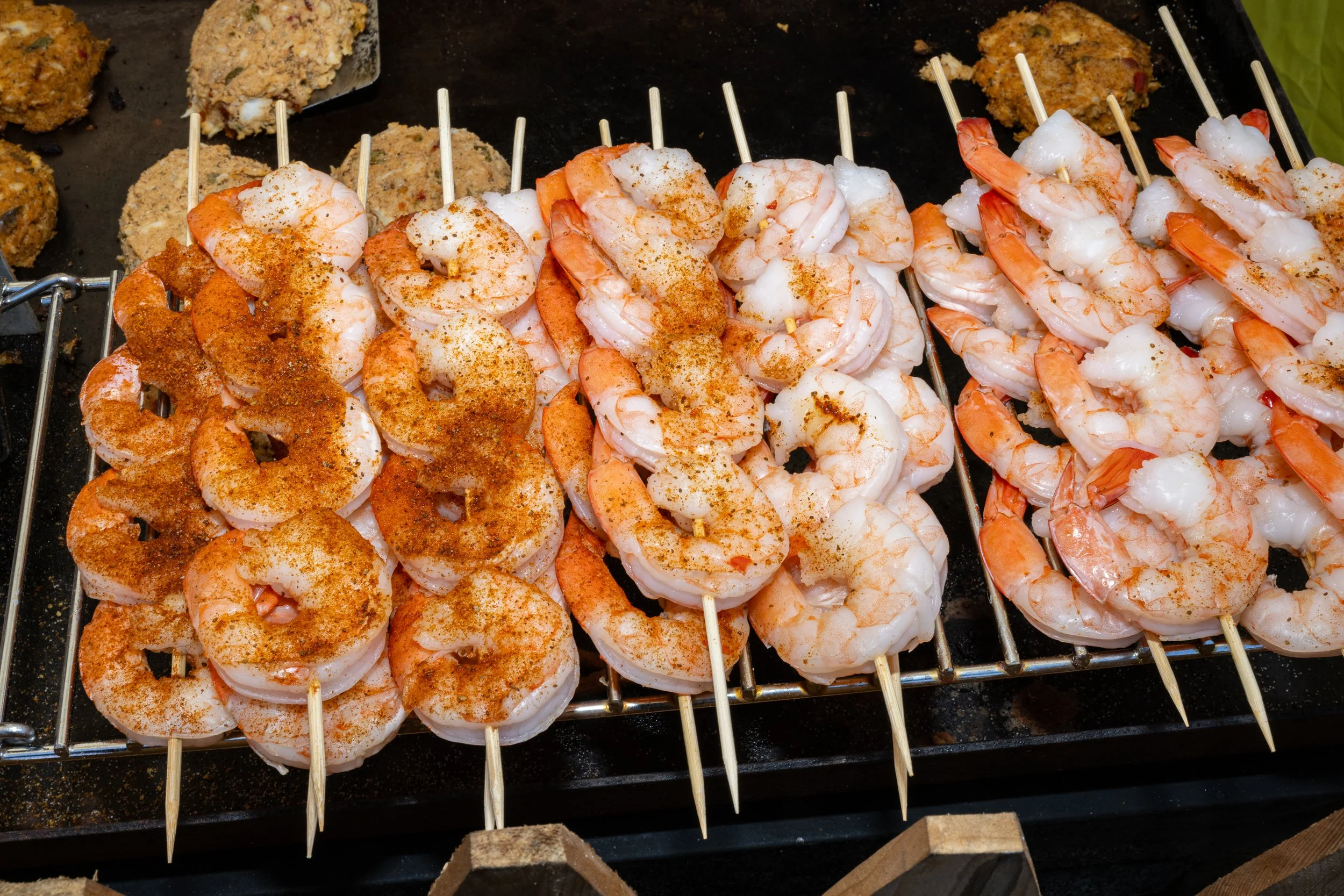 Skewers with cooked shrimp seasoned with spices, lying on a black grilling surface.