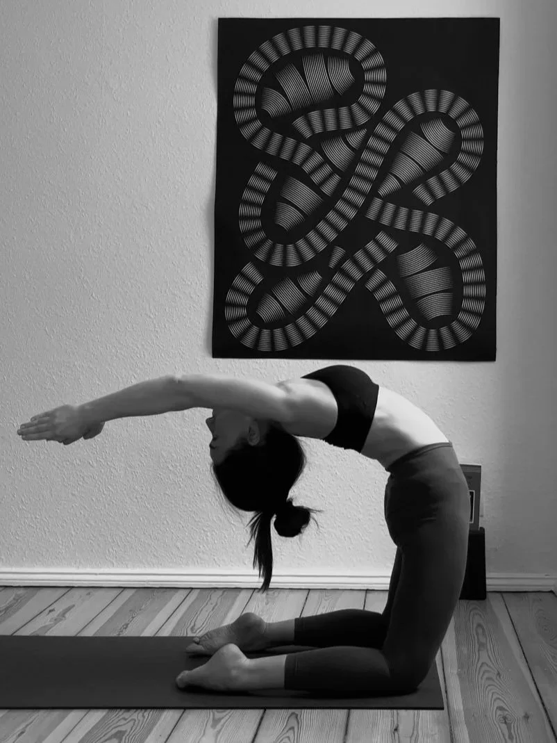 Black and white photograph of private yoga mentor Katharina Fengler in Berlin apartment. Kapotasana preparation picture taken from the side.