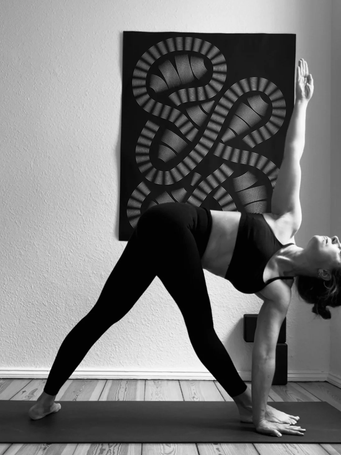 Private Yoga teacher Katharina Fengler demonstrating Trikonasana B in front of abstract art in Berlin apartment. 