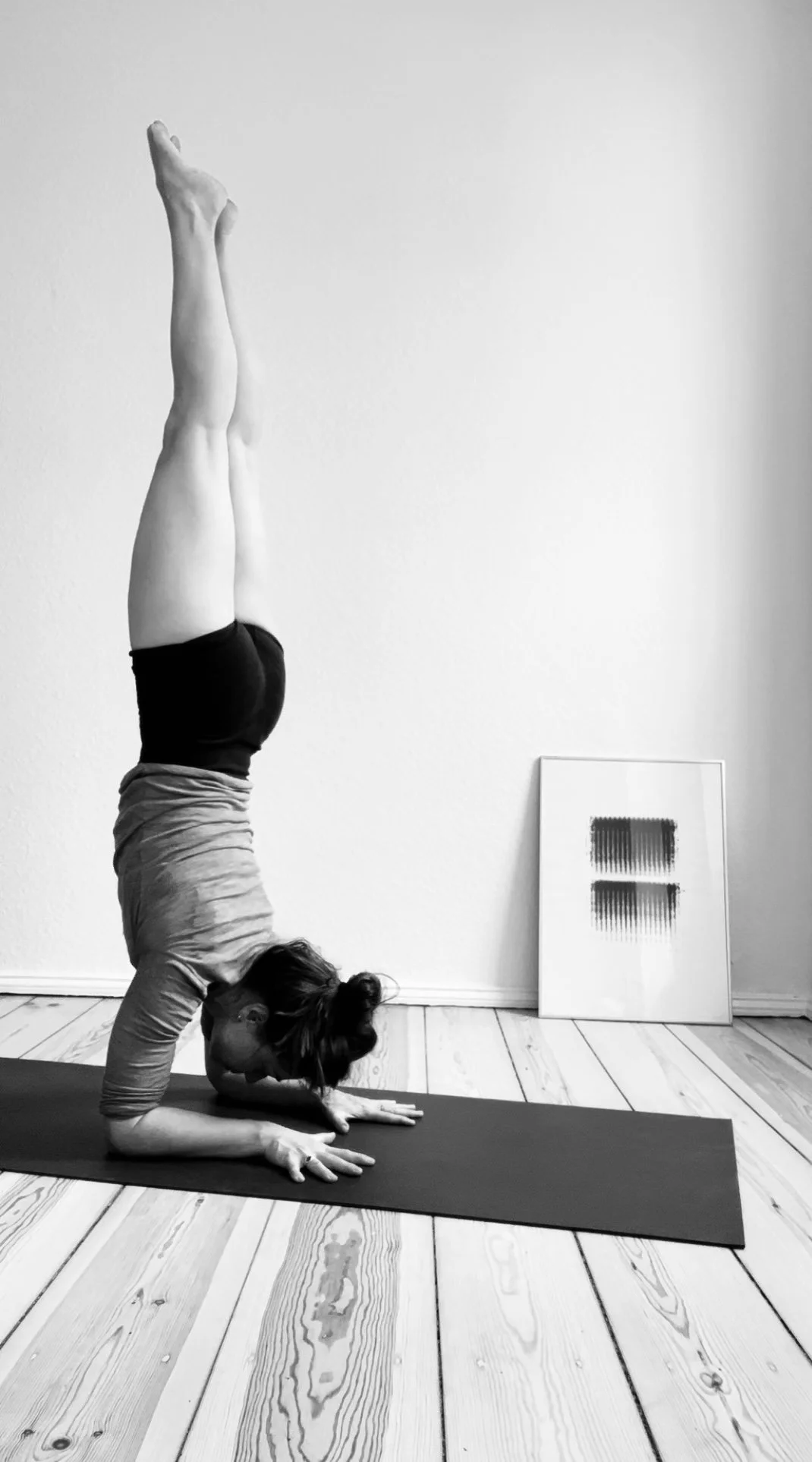 Private Yoga teacher Katharina Fengler demonstrating Pincha Mayurasana in Berlin apartment with abstract art in background