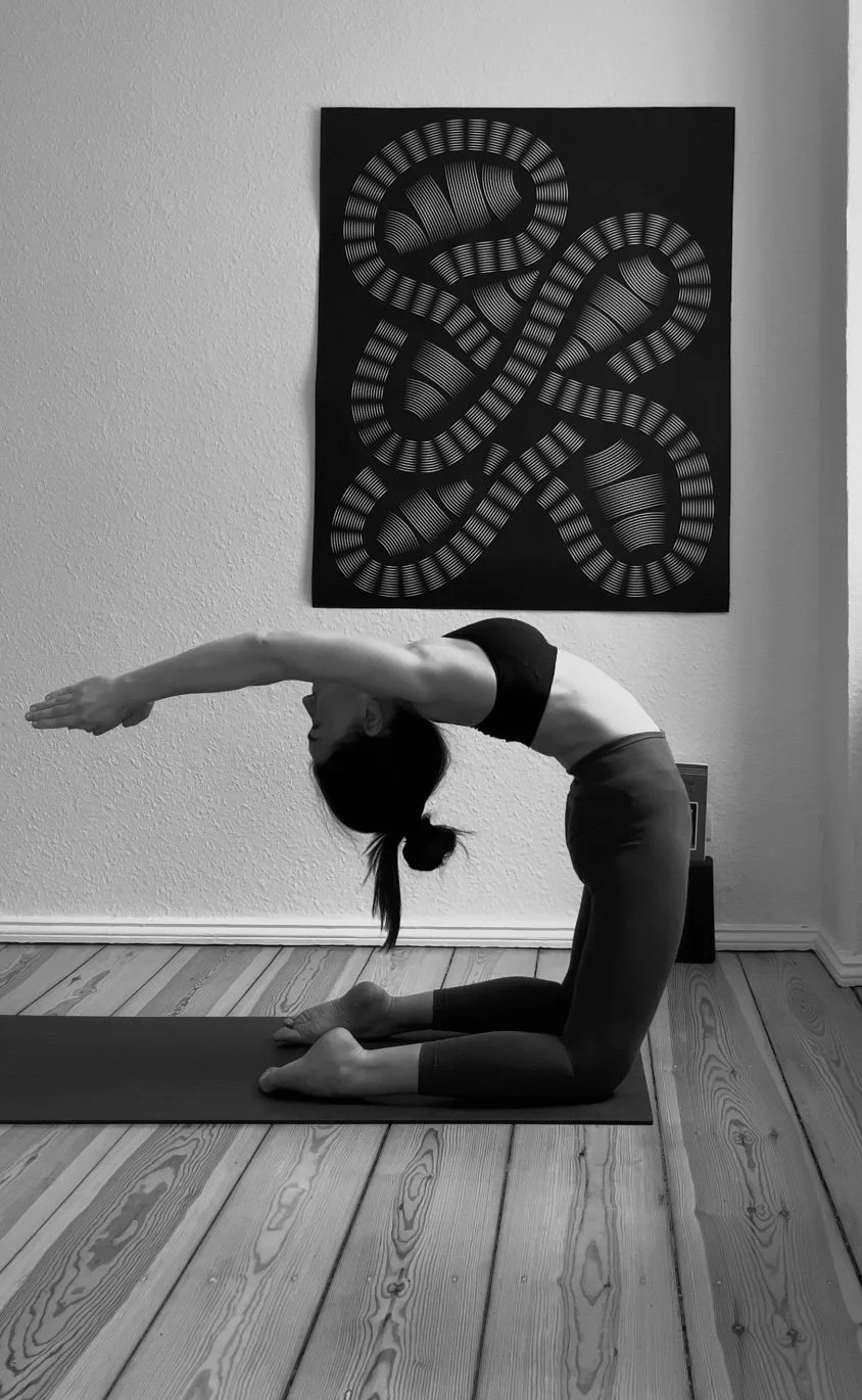 Black and white photograph of private yoga mentor Katharina Fengler in Berlin apartment. Kapotasana preparation picture taken from the side.