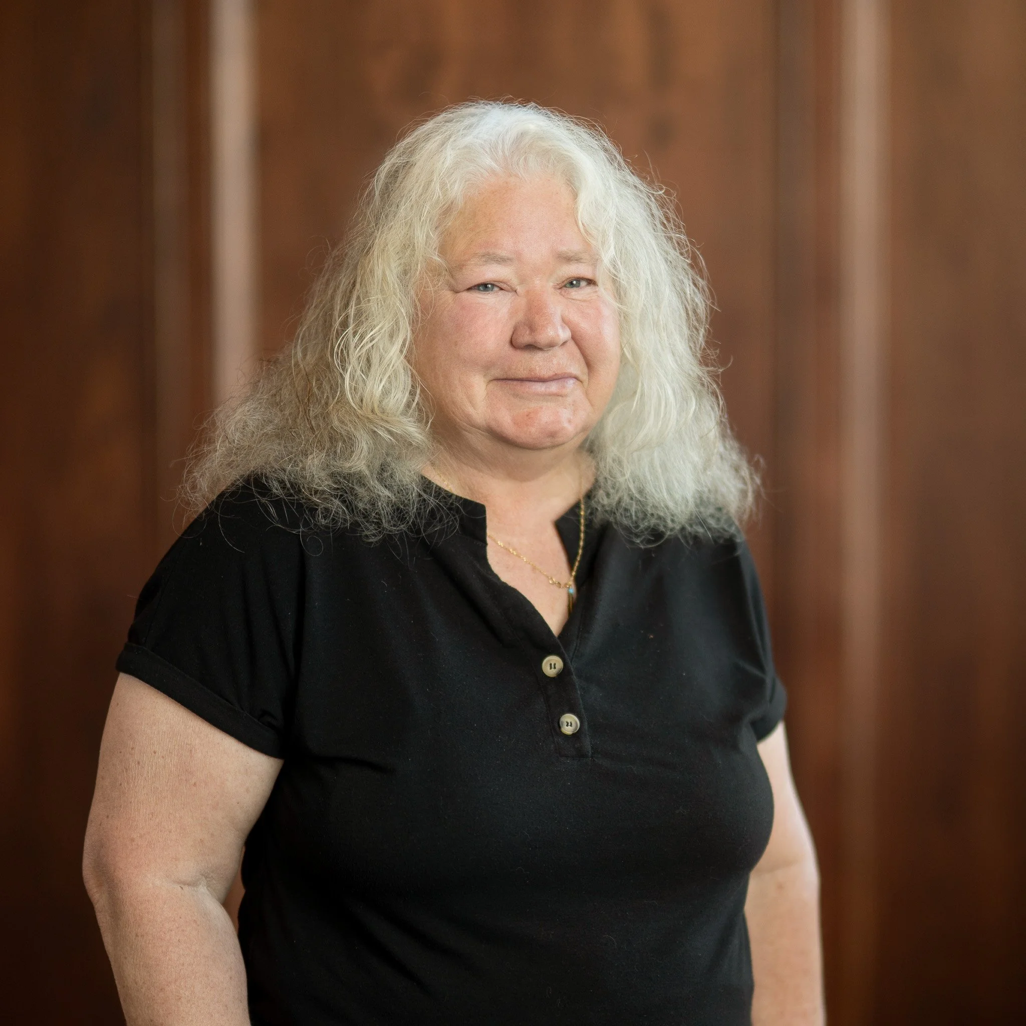 A woman with shoulder length curly gray hair  and a black collared shirt