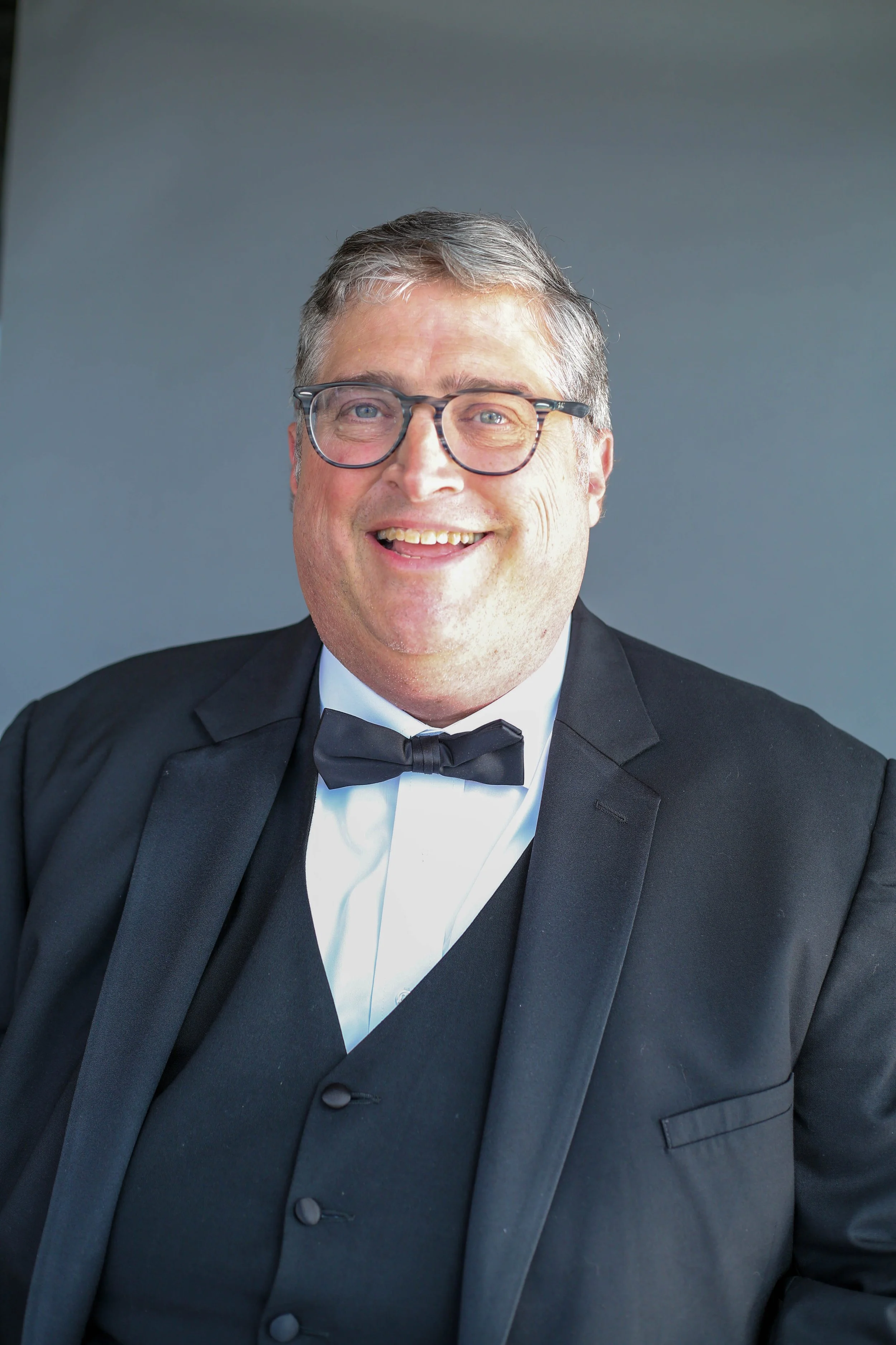 A man wearing glasses and a tuxedo smiling at the camera.