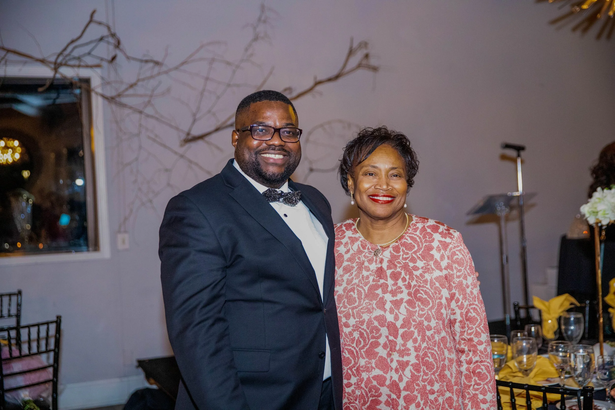 A smiling man in a tuxedo and a woman in a patterned dress at a formal event.