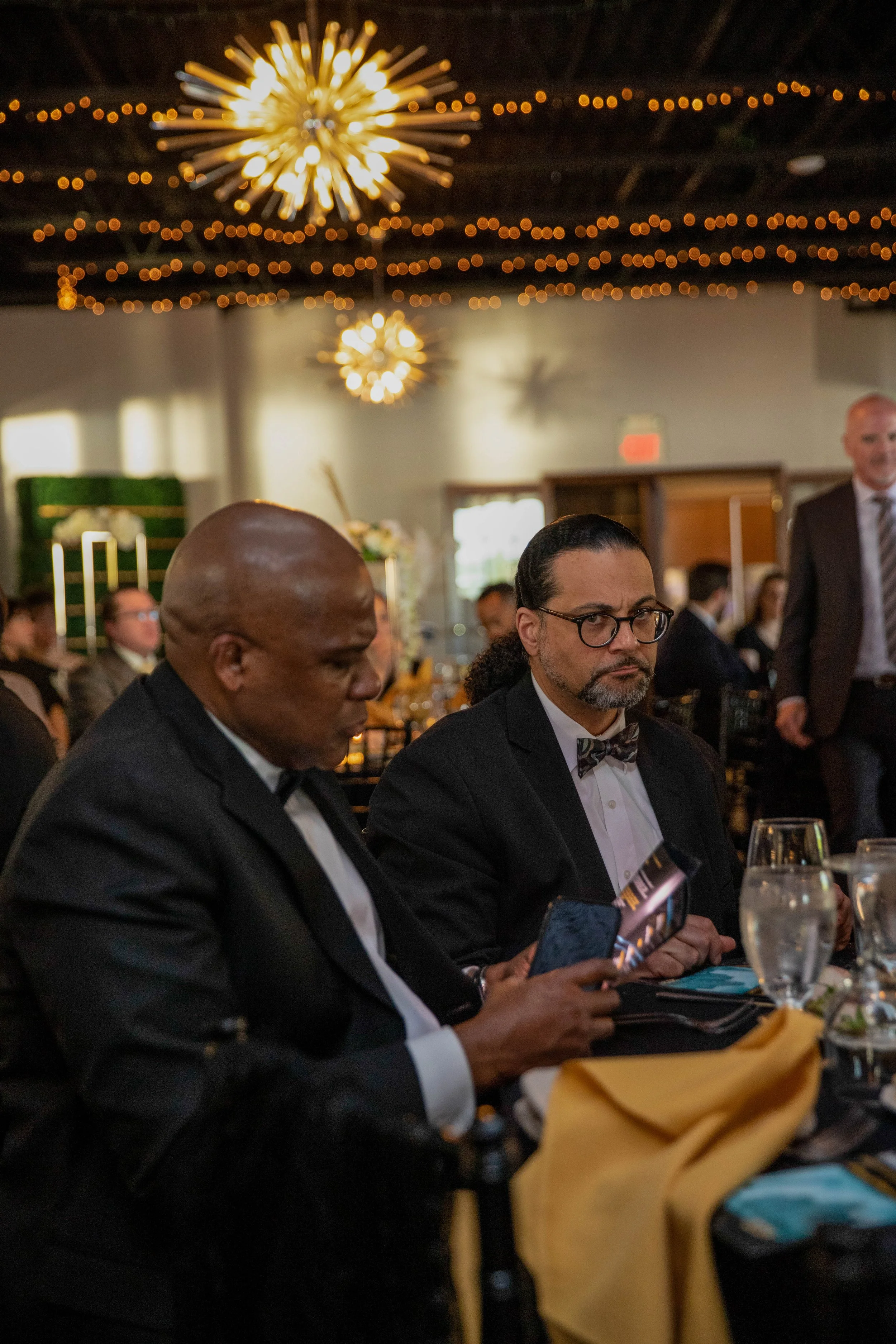 People in formal attire attending a dinner event with sparklers and string lights hanging from the ceiling.