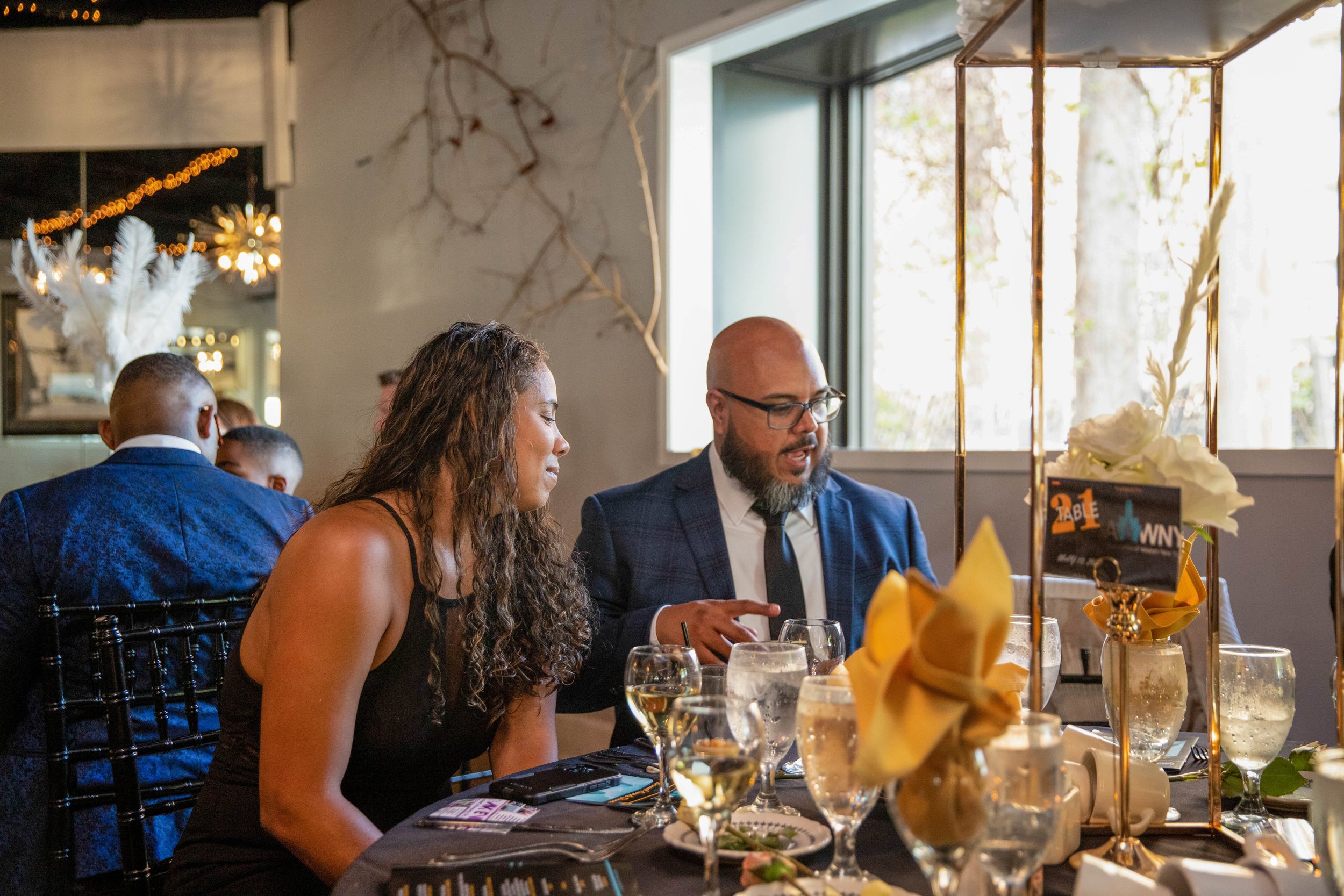 People sitting at a dining table in a restaurant, enjoying a meal, with a decorative centerpiece and glasses of beverages.