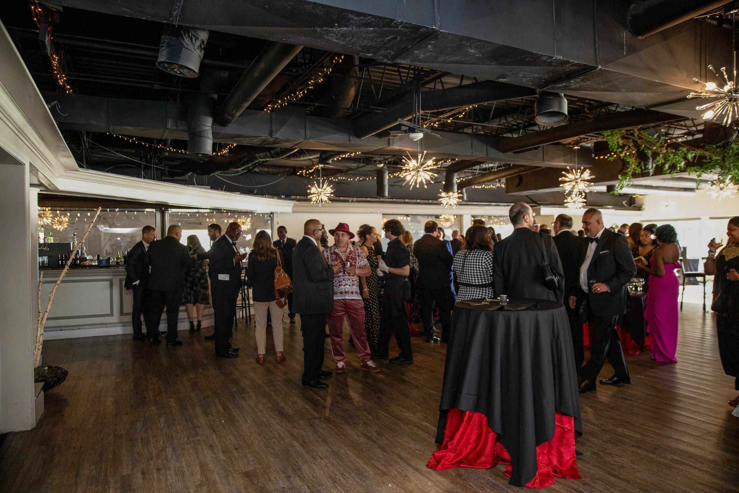 People dressed in formal attire socializing at an indoor event with decorative lighting and modern decor.