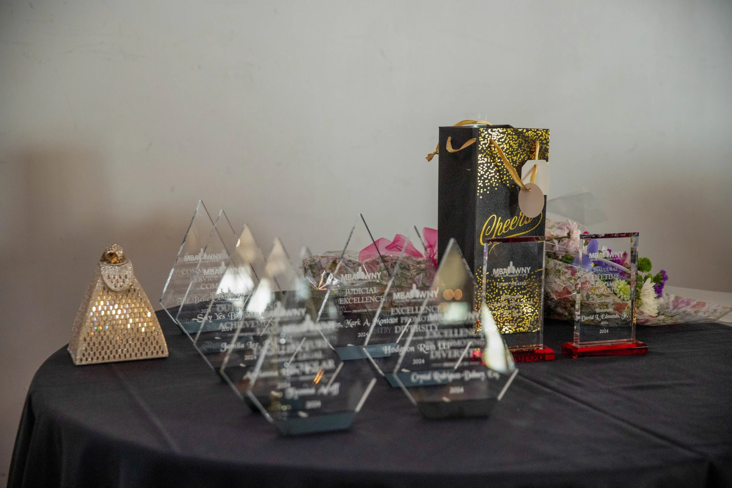 A table displaying various awards and trophies, including plaques, trophies, and a decorative golden object, with a plain white wall in the background.