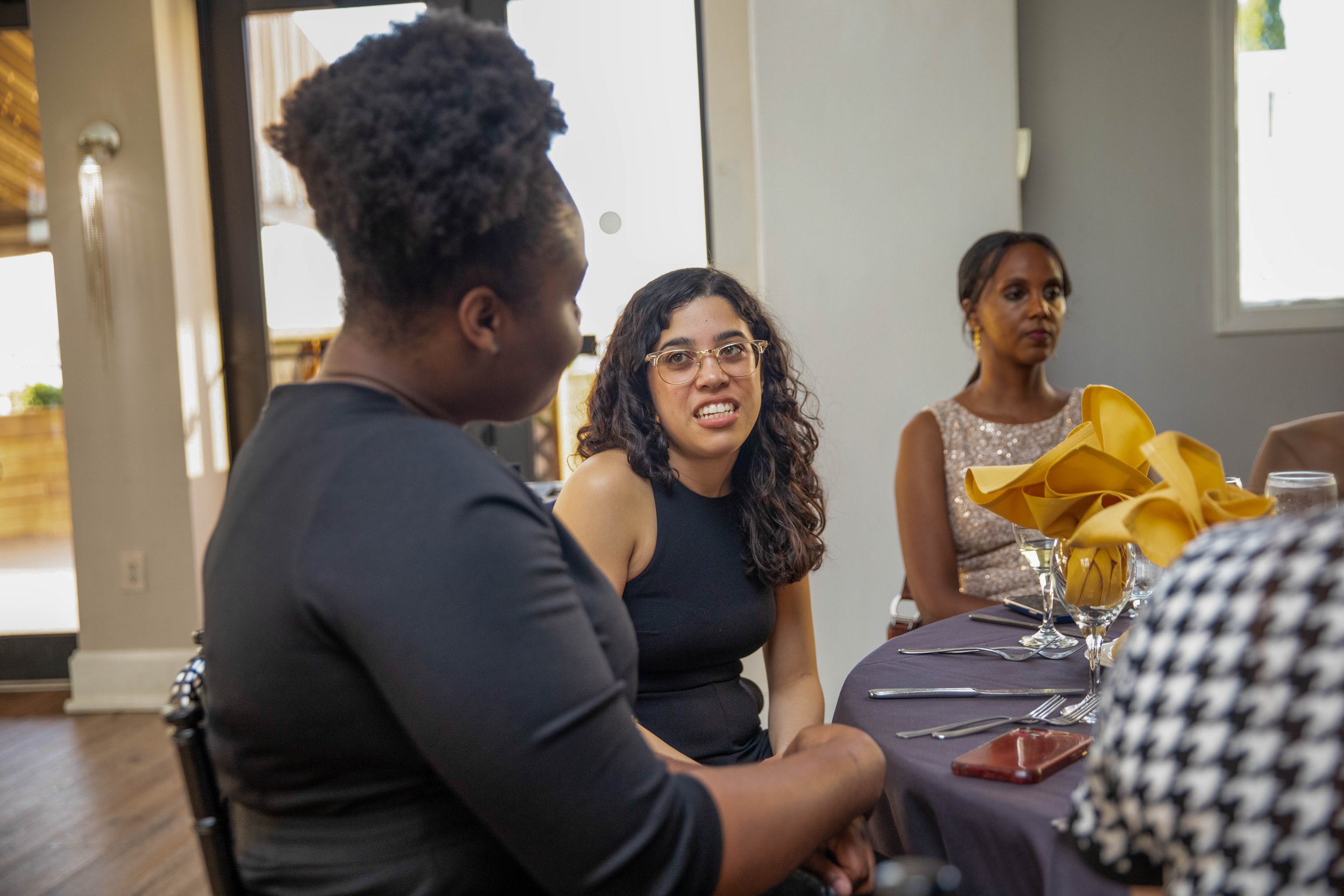 A group of diverse women sitting at a table during a social gathering or celebration, engaged in conversation.