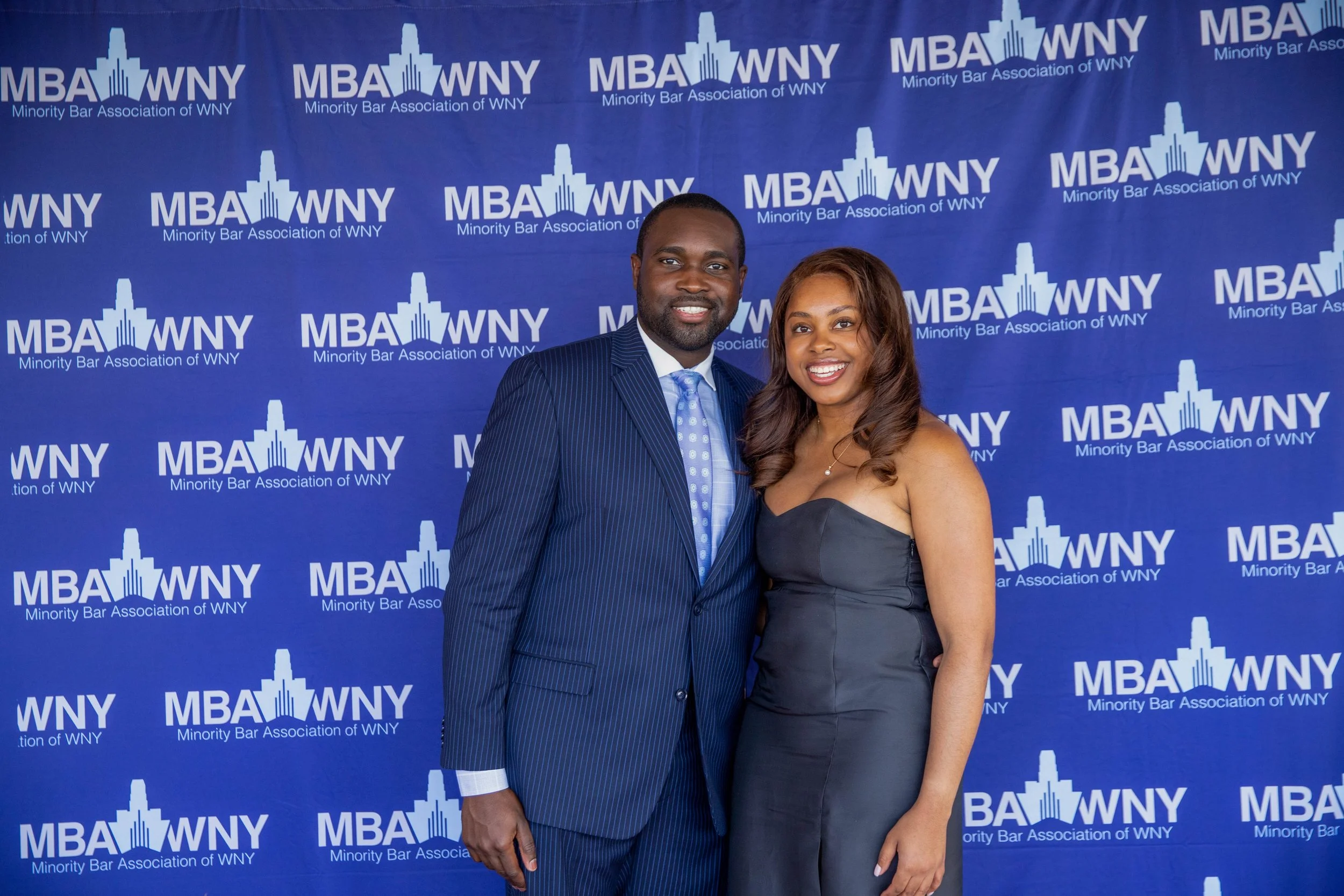 A man and woman standing together, smiling at the camera at an event for the Minority Bar Association of WNY. The background displays the organization's logo.