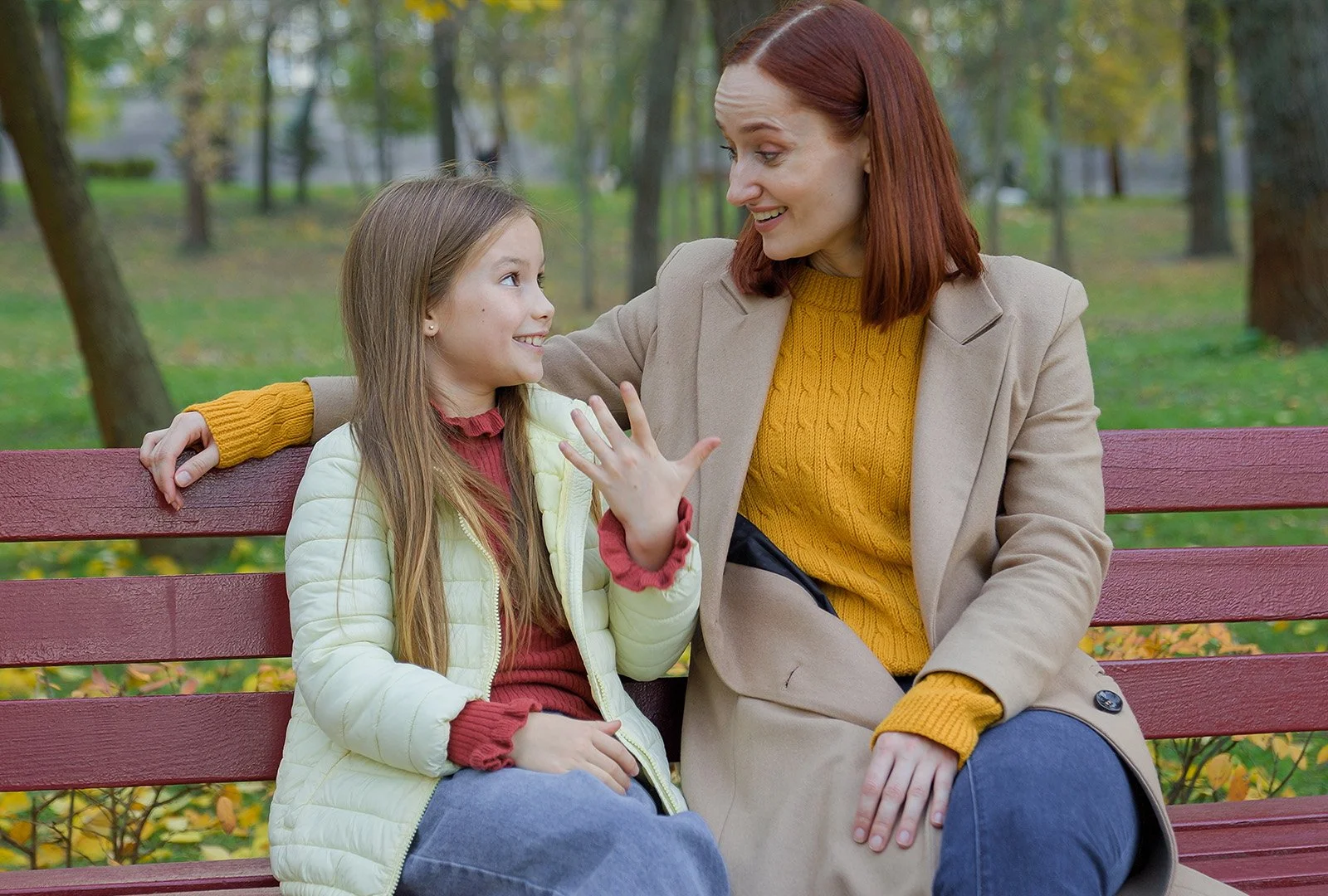 Mom and young daughter sit on a park bench to have a chat.