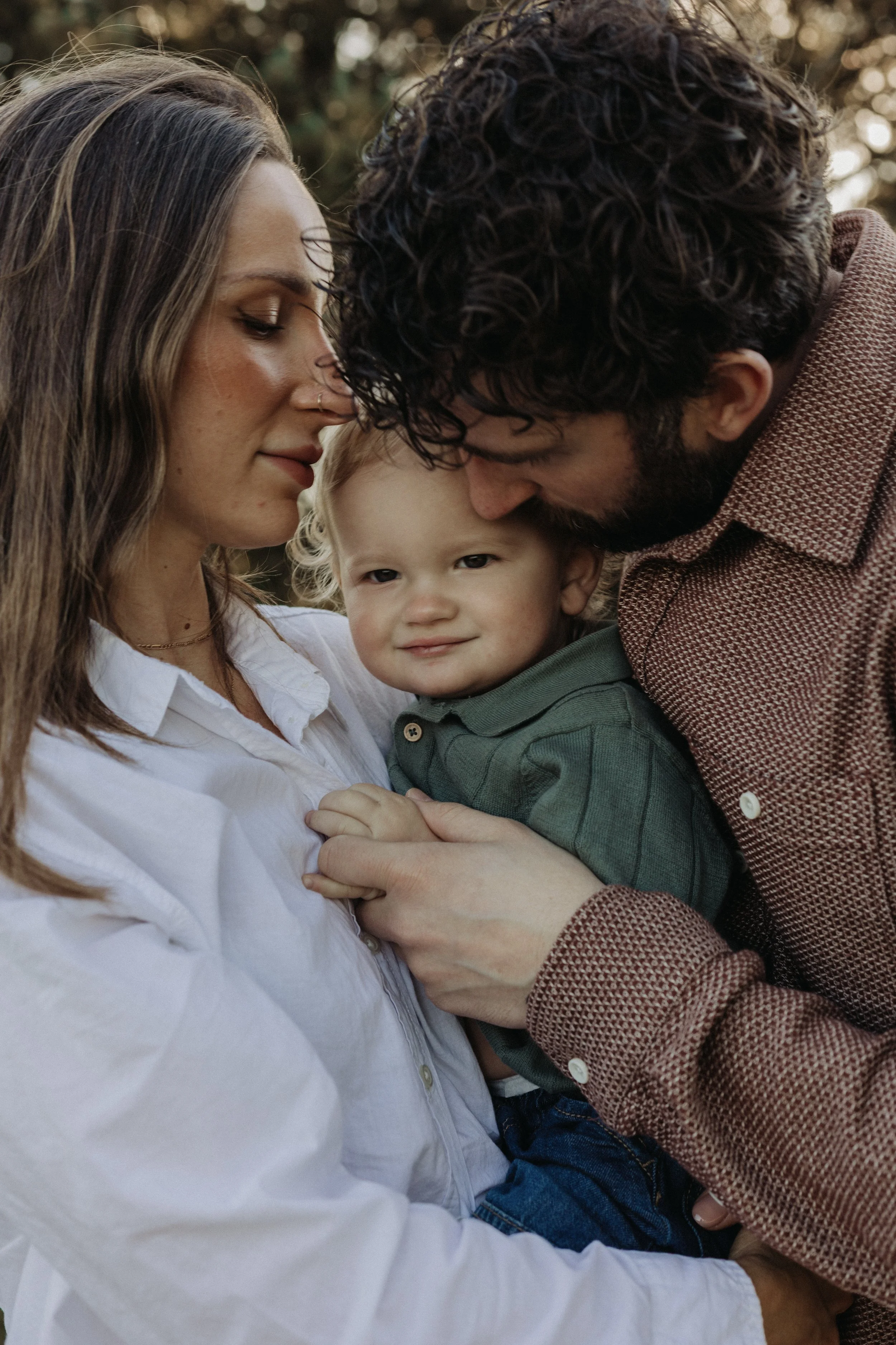 A close-up of a happy family moment showing a woman, a man, and a young boy, with the woman and man touching foreheads and the boy smiling.