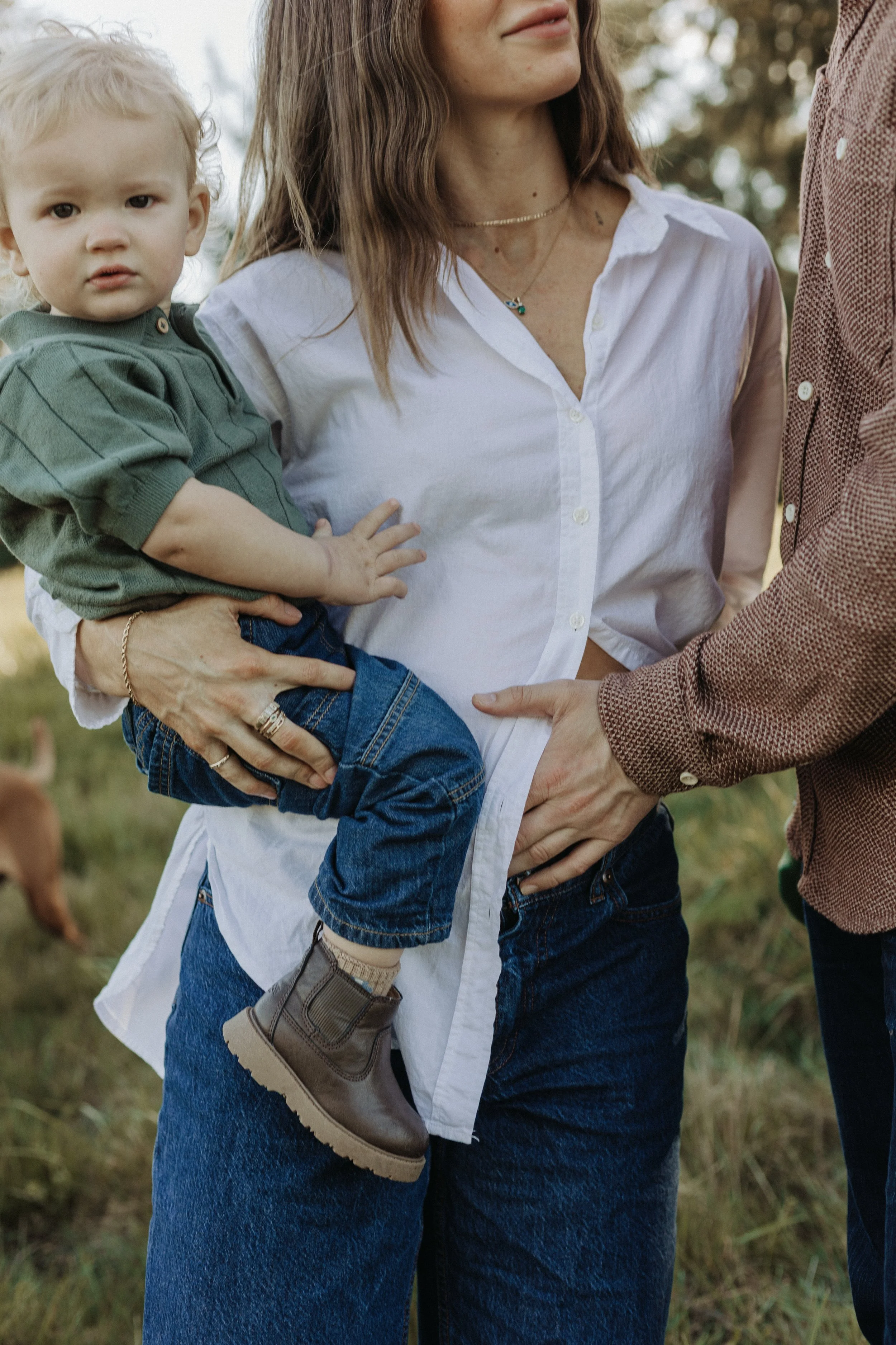 A woman holding a young boy on her hip, with two adults standing nearby. The scene is outdoors in a natural setting, possibly a park or field.