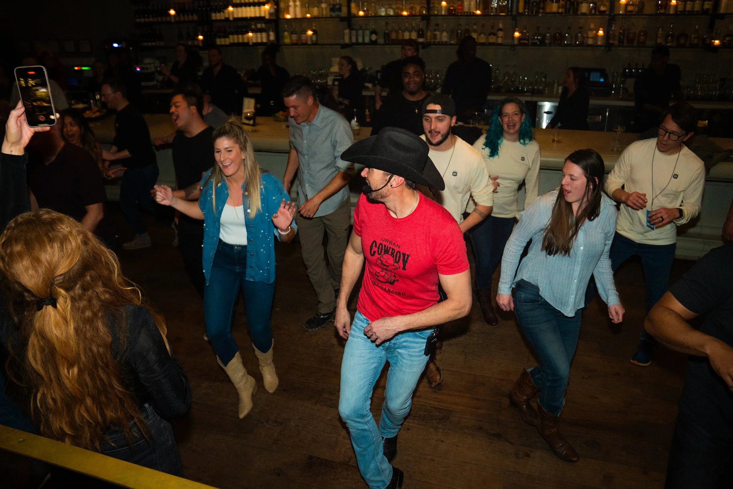 A group of people dancing and having fun at a party in a dimly lit bar or nightclub. Some are smiling and the atmosphere appears lively.