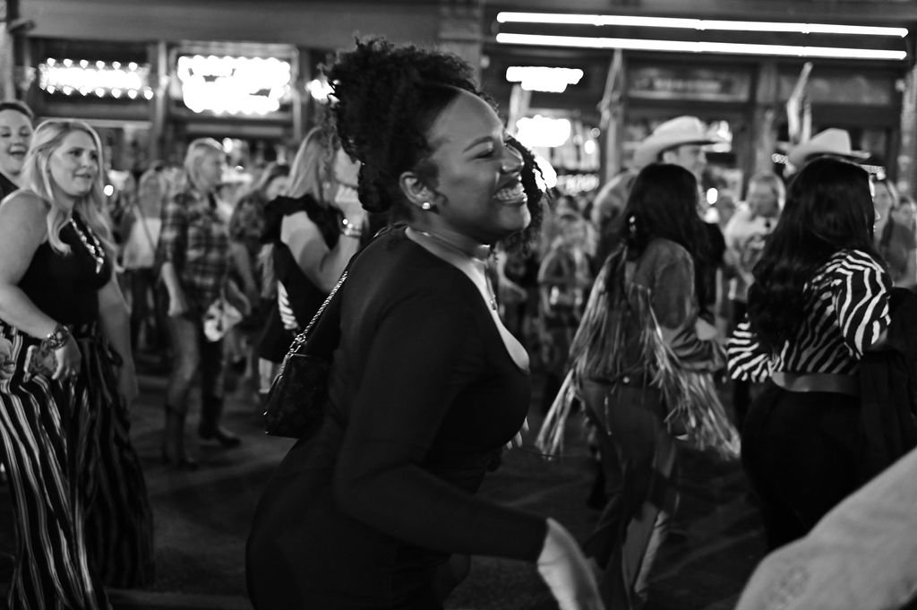 A group of women dancing and having fun at a lively indoor event or party, some wearing striped and patterned outfits.