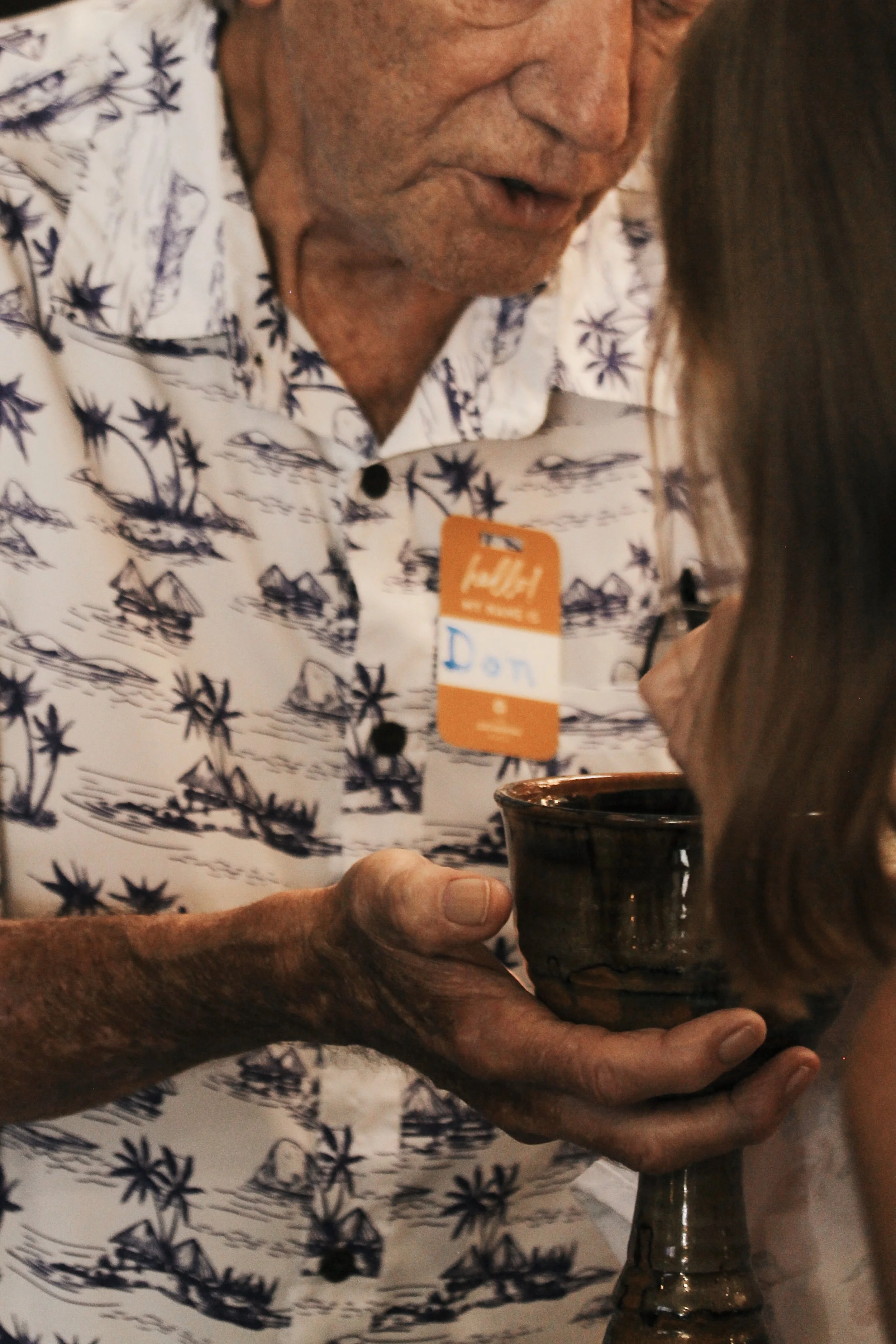 Close-up of an elderly man handing a young girl a ceramic cup at a gathering, both partially visible.