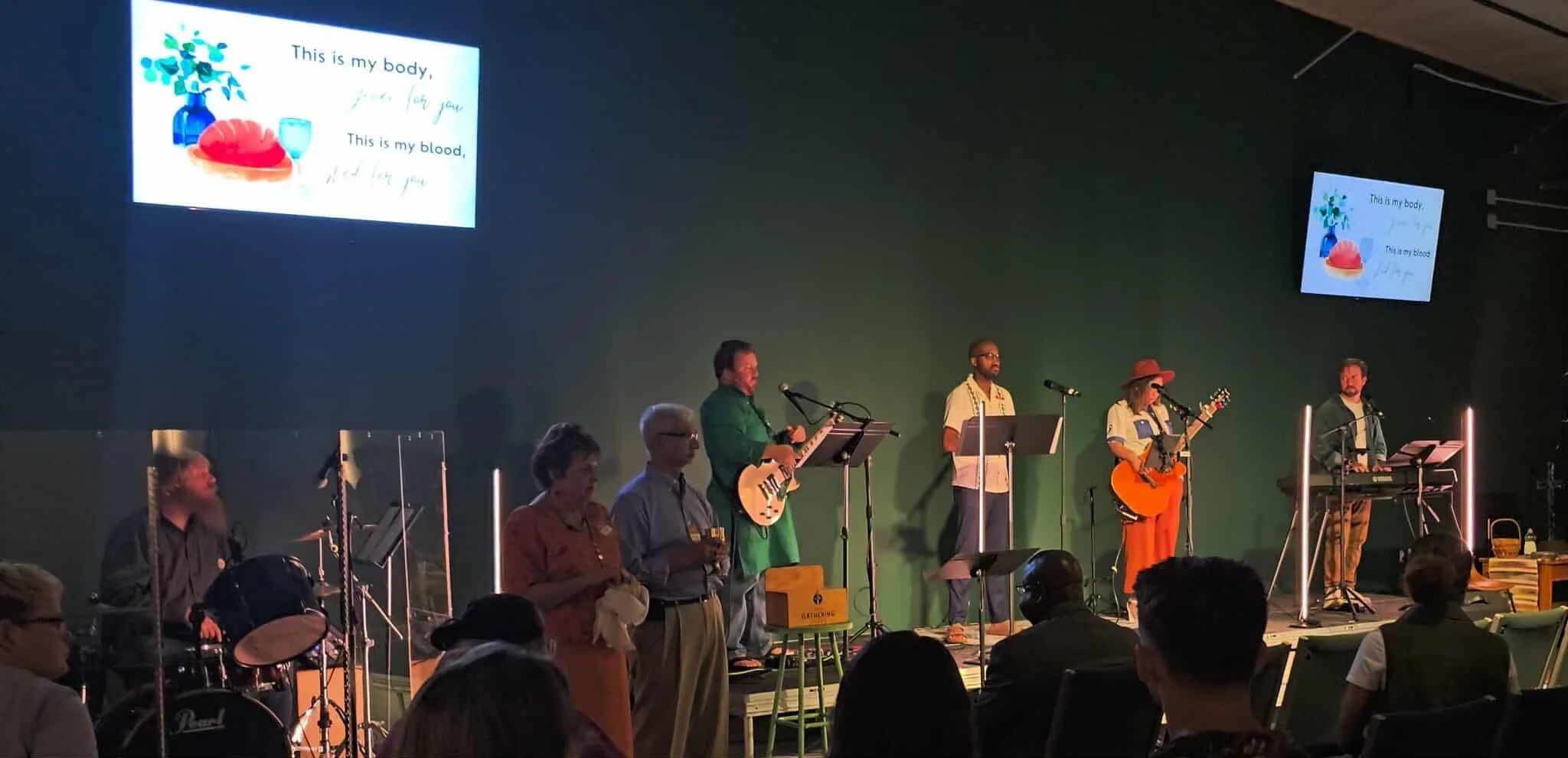 People sitting in a row at an indoor event, with some appearing to be praying or meditating, mostly with eyes closed and heads bowed.