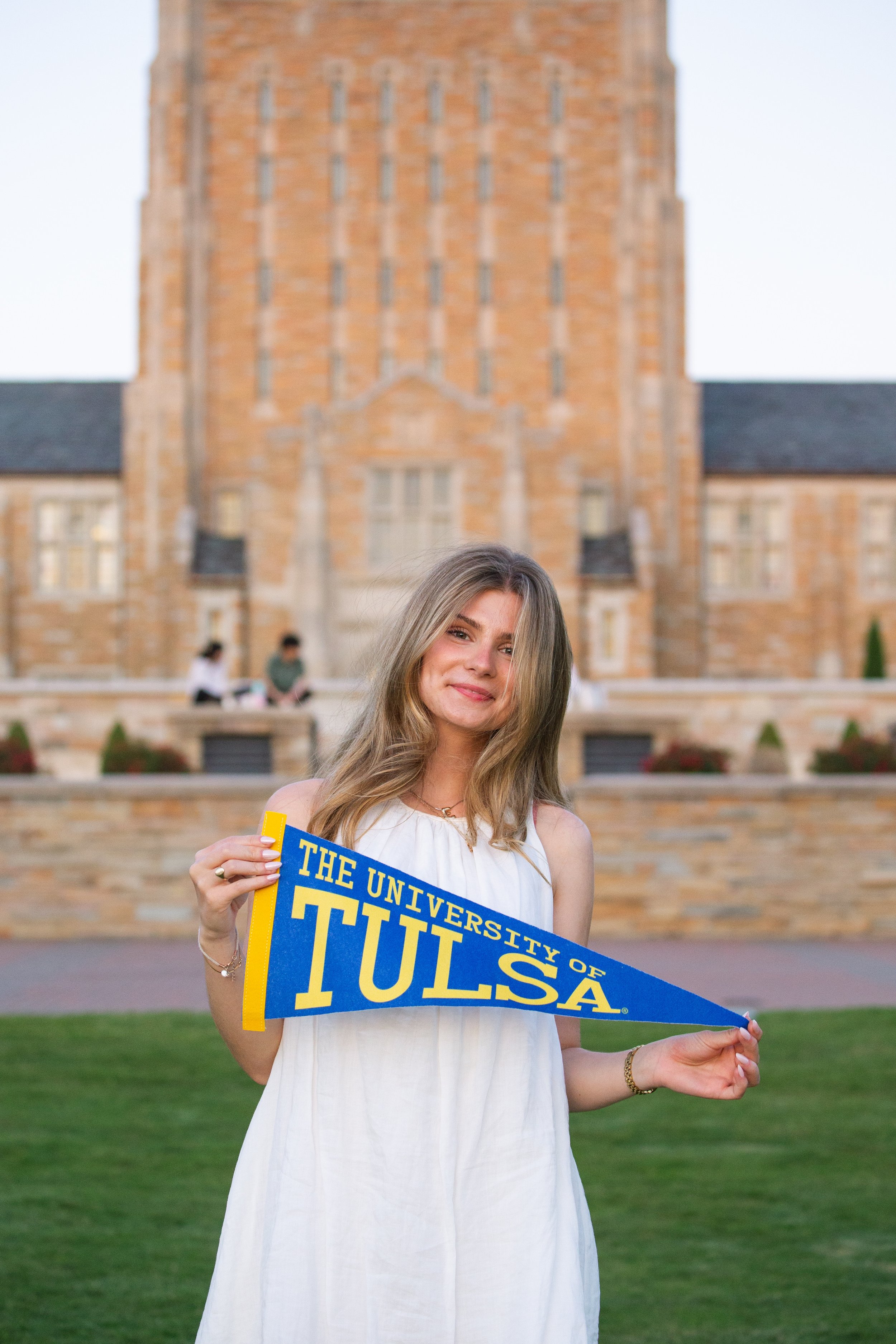 A woman in a white dress holding a TU flag smiles in front of McFarlin Library