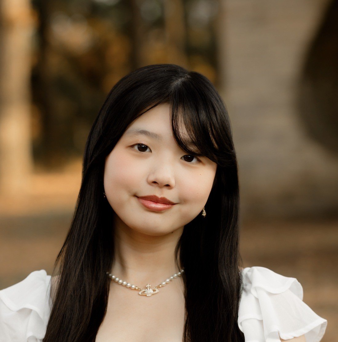 Bella has long black hair, a white shirt, and smiles softly directly into the camera