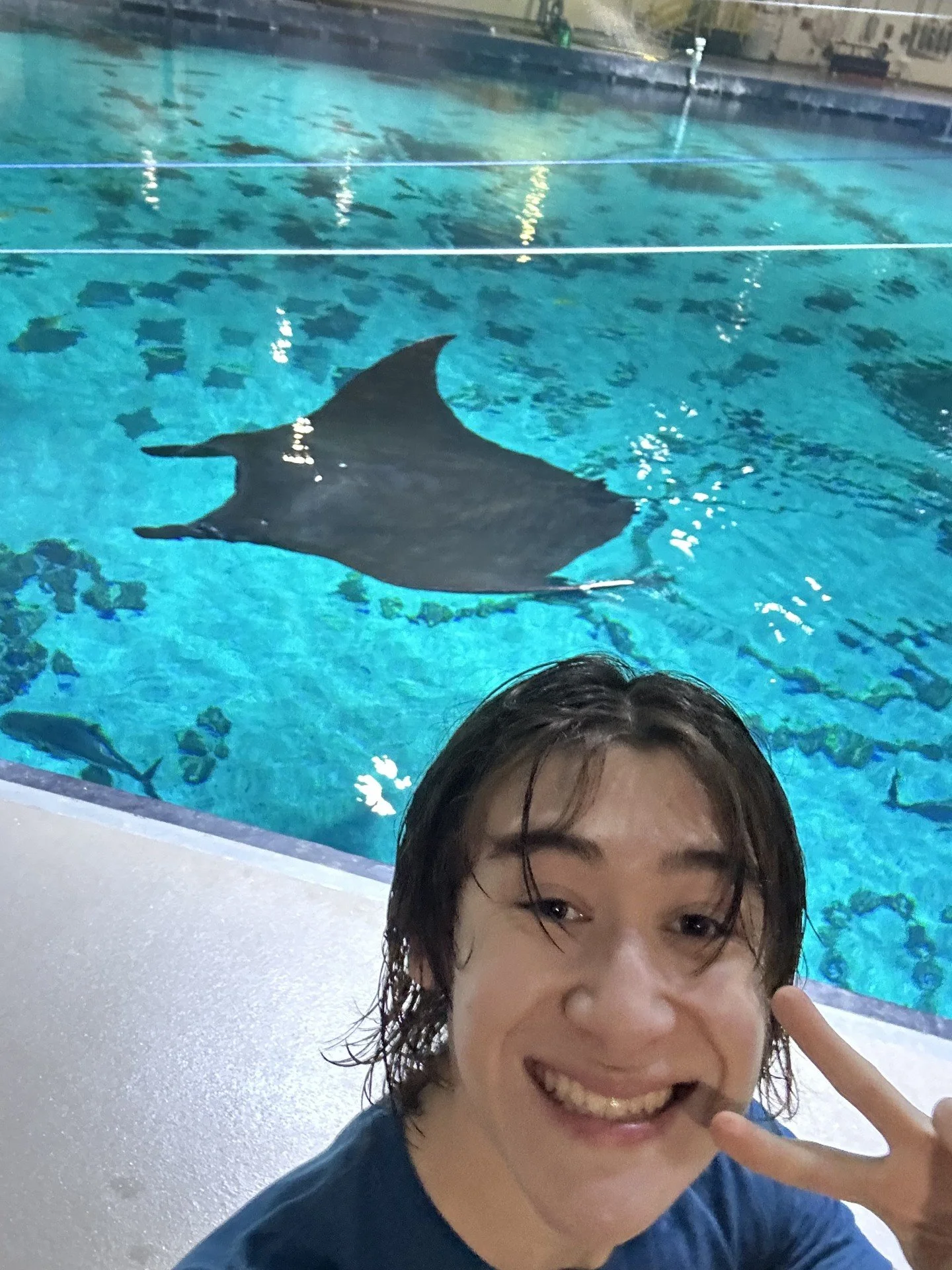 Drew smiles and gives a peace sign a the camera with a manta ray in the background