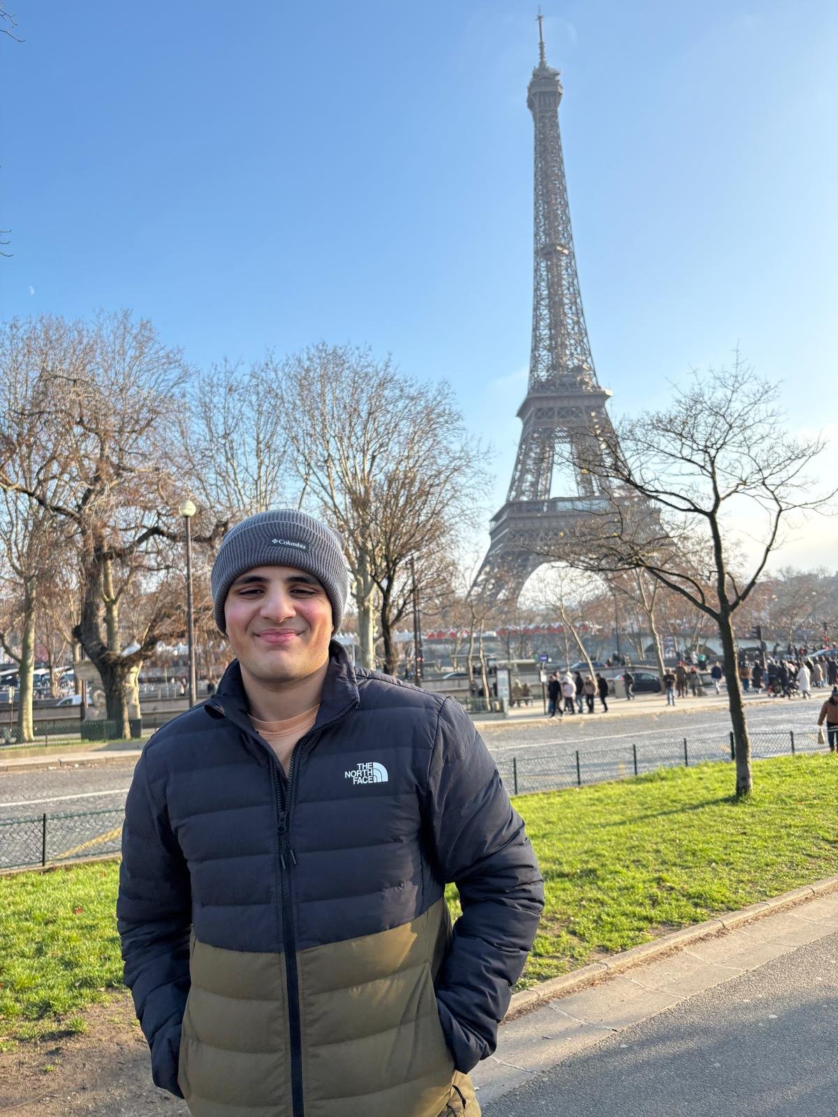 A man in a hat smiles in front of the Eiffel Tower.