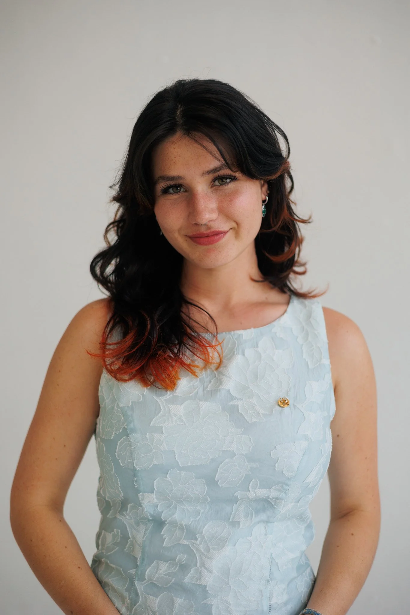 A woman with long dark hair and a white shirt smiles at the camera in front of a white wall.