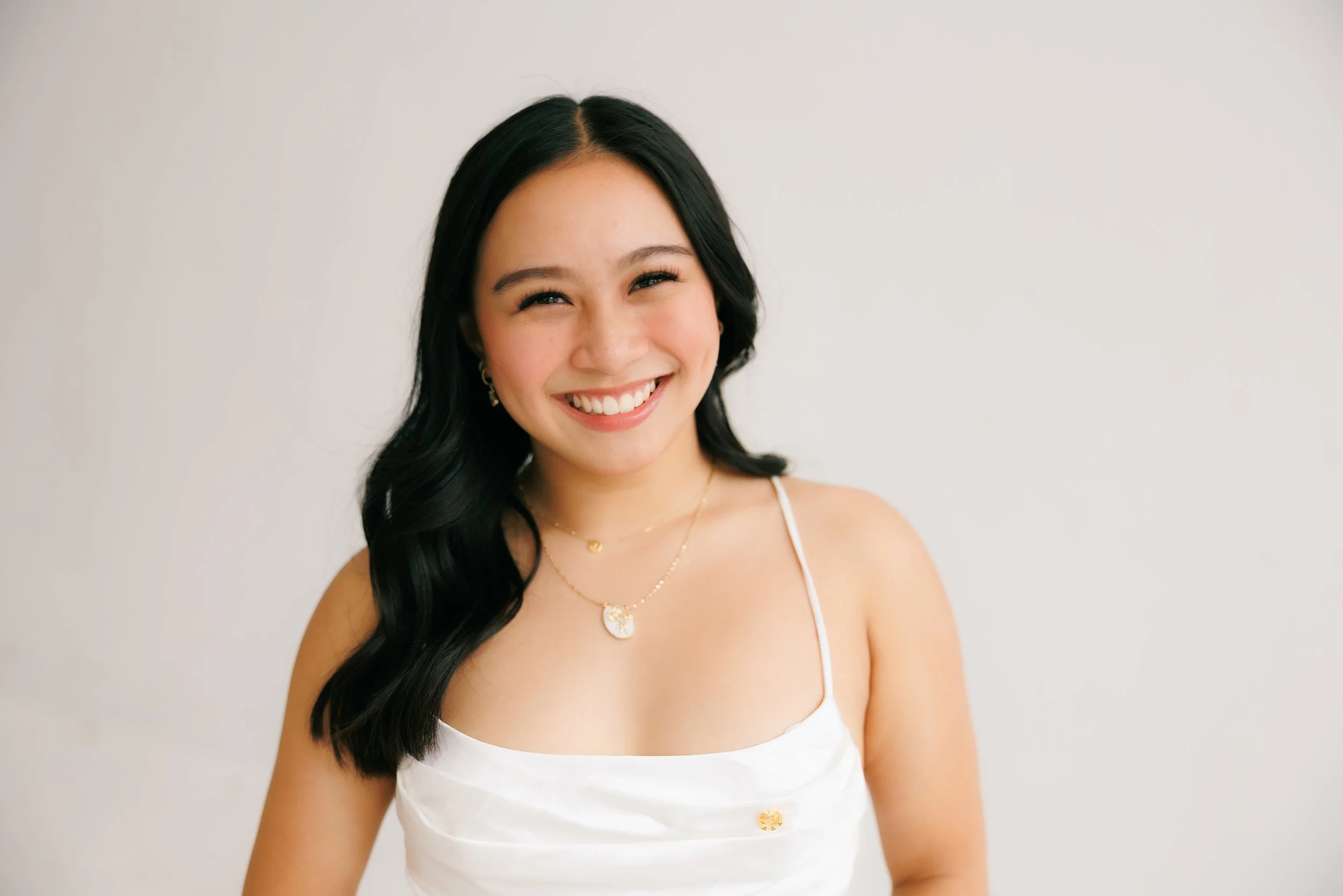 A woman with long dark hair and a white shirt smiles at the camera