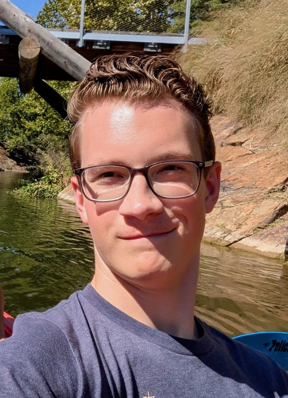 A man with short blond hair and glasses smiles into the camera in front of a river