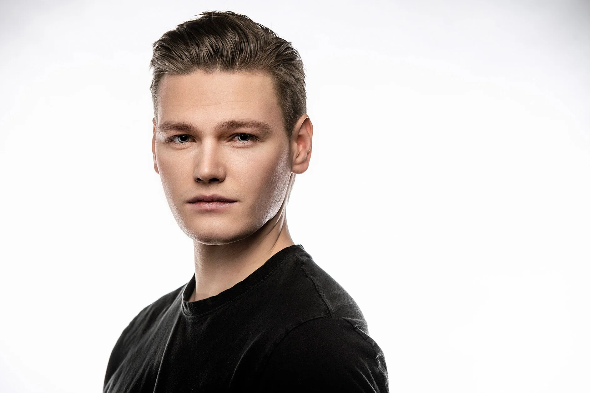 A young man with styled hair, wearing a black shirt, posing against a plain light background.
