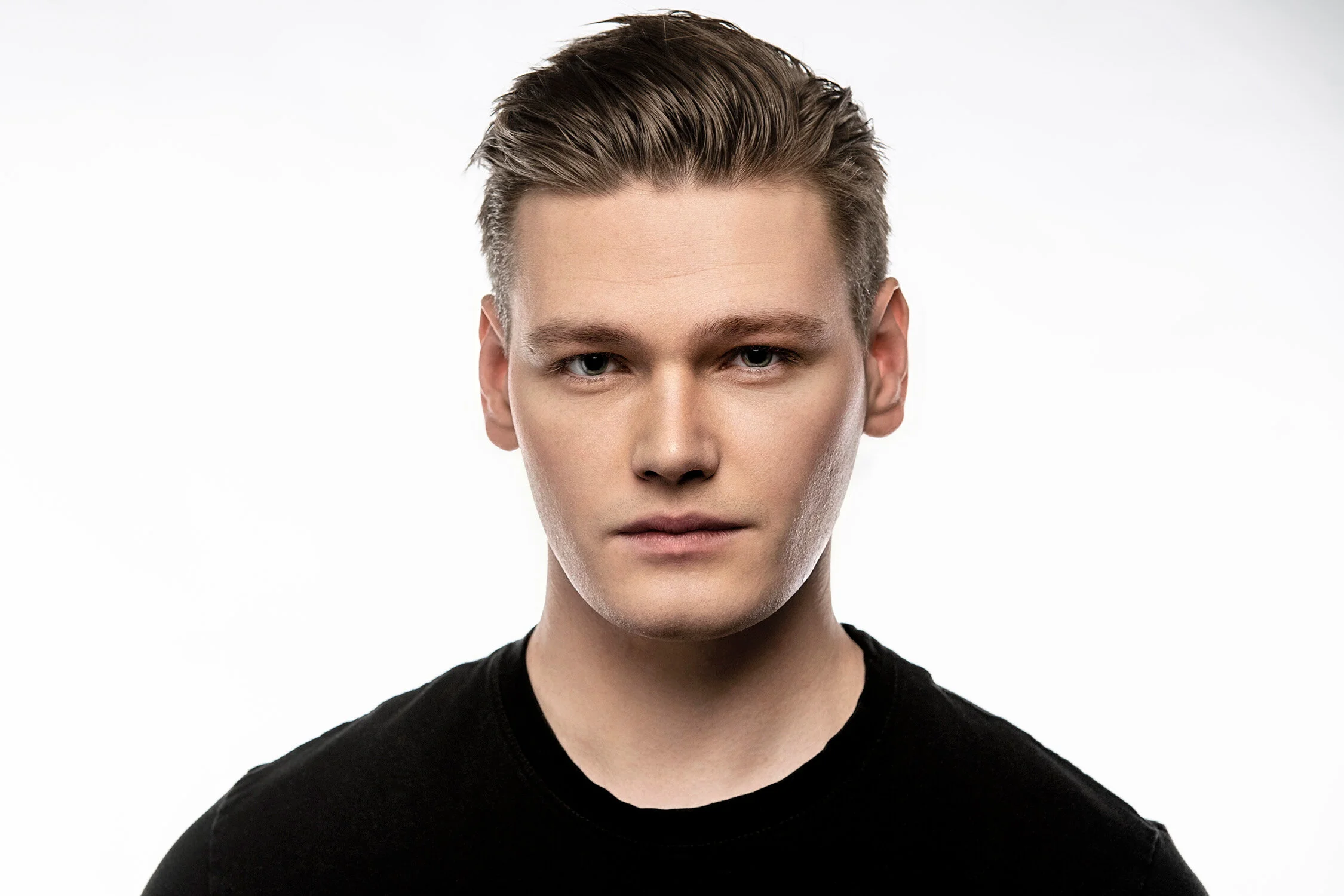Portrait of a young man with slicked-back hair, wearing a black shirt, against a plain white background.
