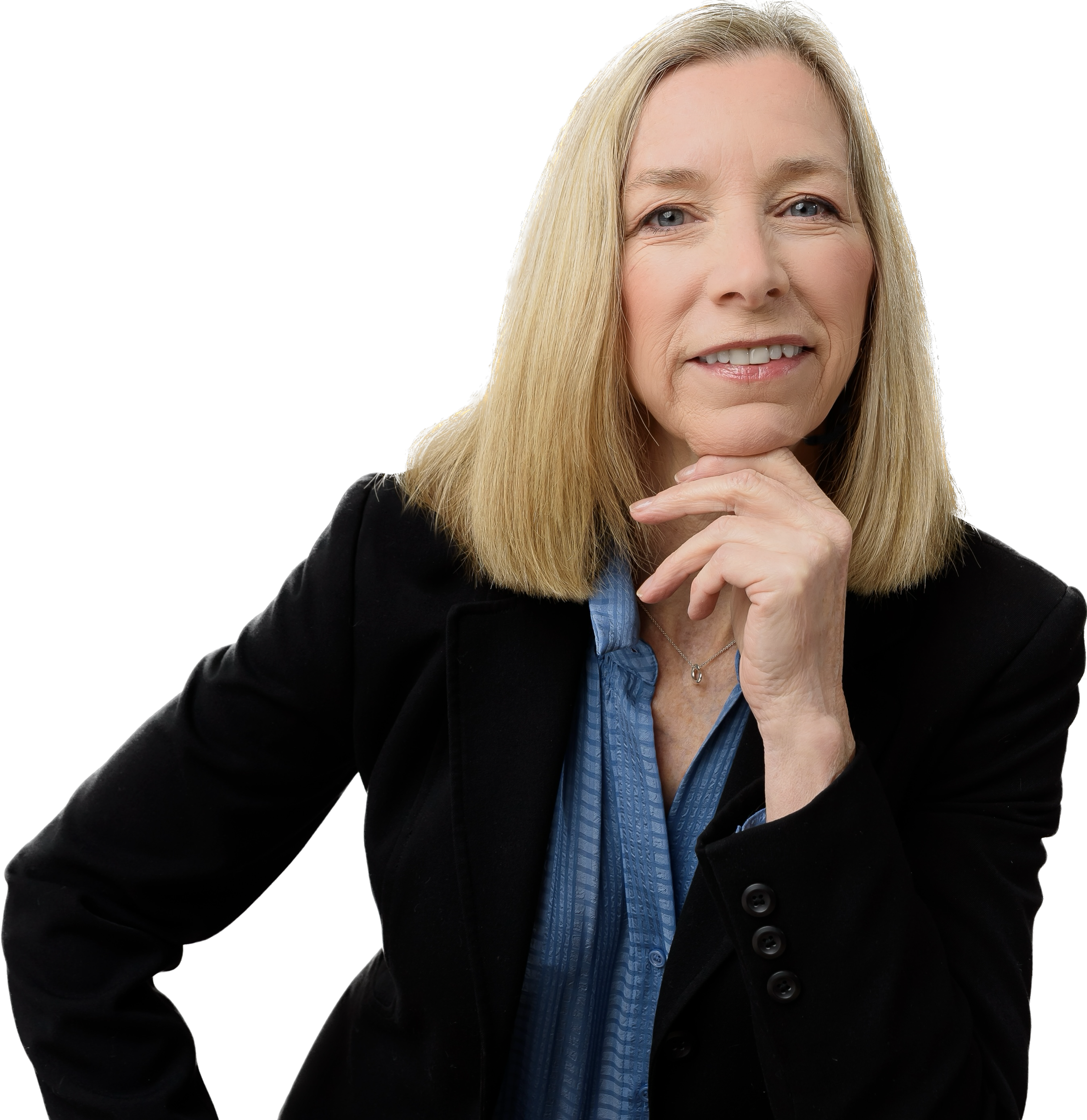 A middle-aged woman with blonde hair and blue eyes smiling, wearing a black blazer and blue blouse, with her chin resting on her hand.