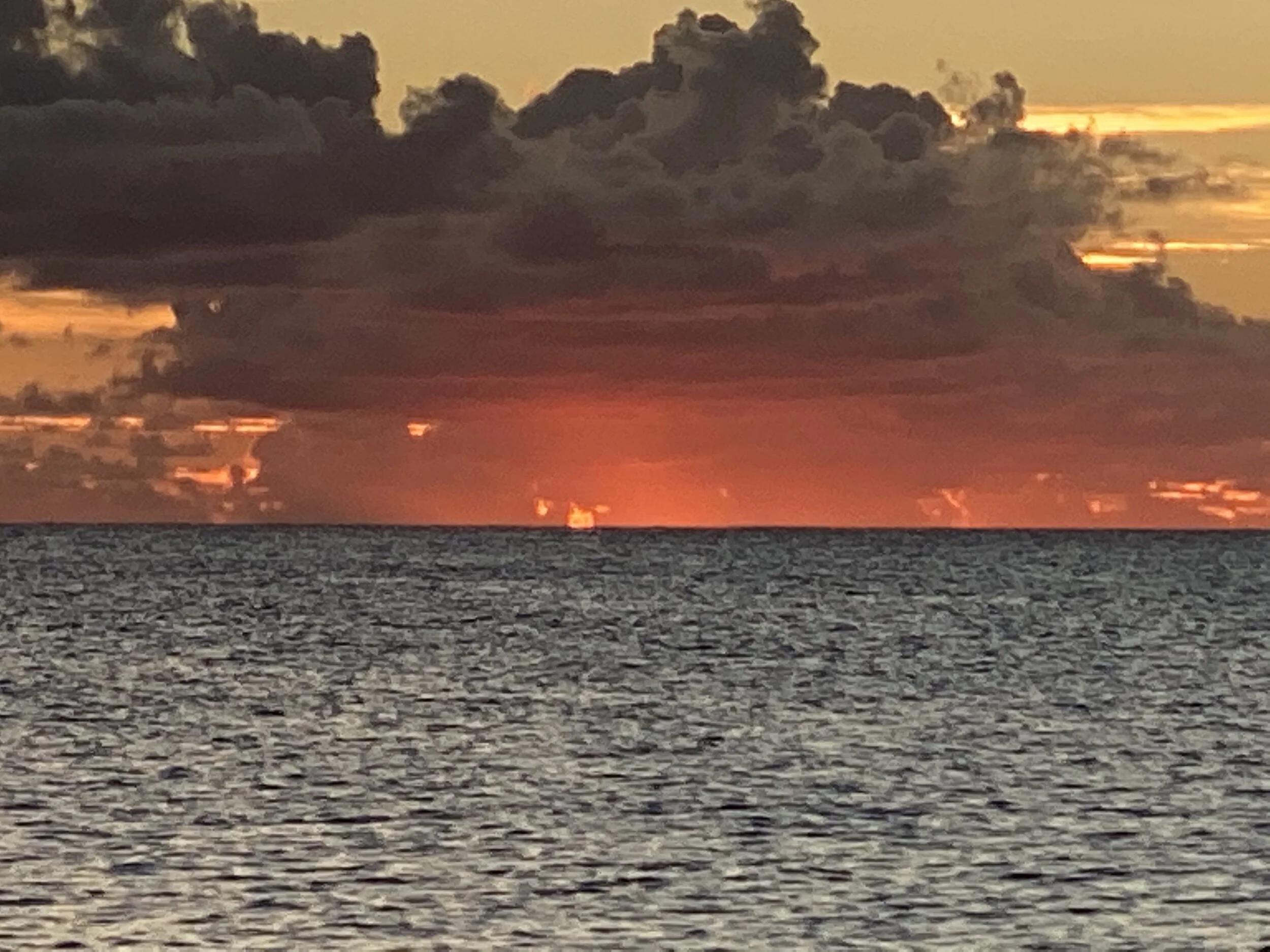 Ocean at sunset with dark clouds and orange sky.