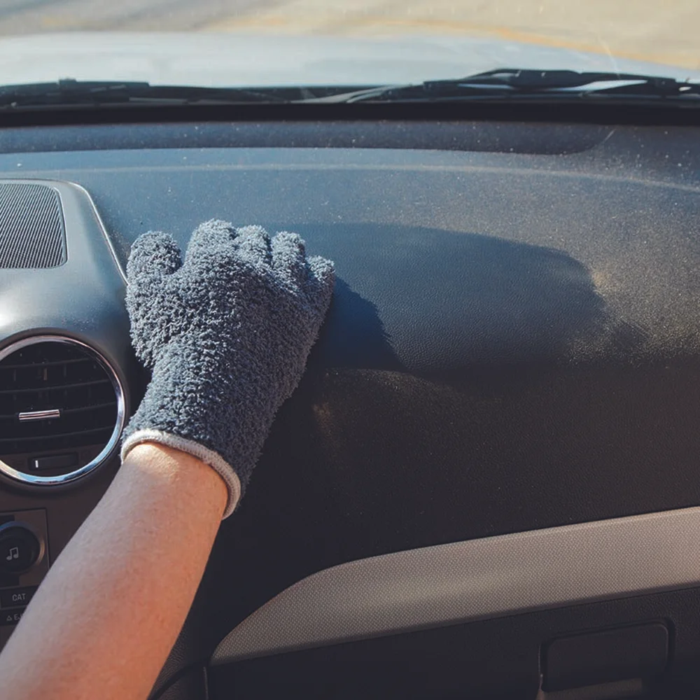 Person wearing a gray and white glove cleaning the dashboard of a car with a cloth.