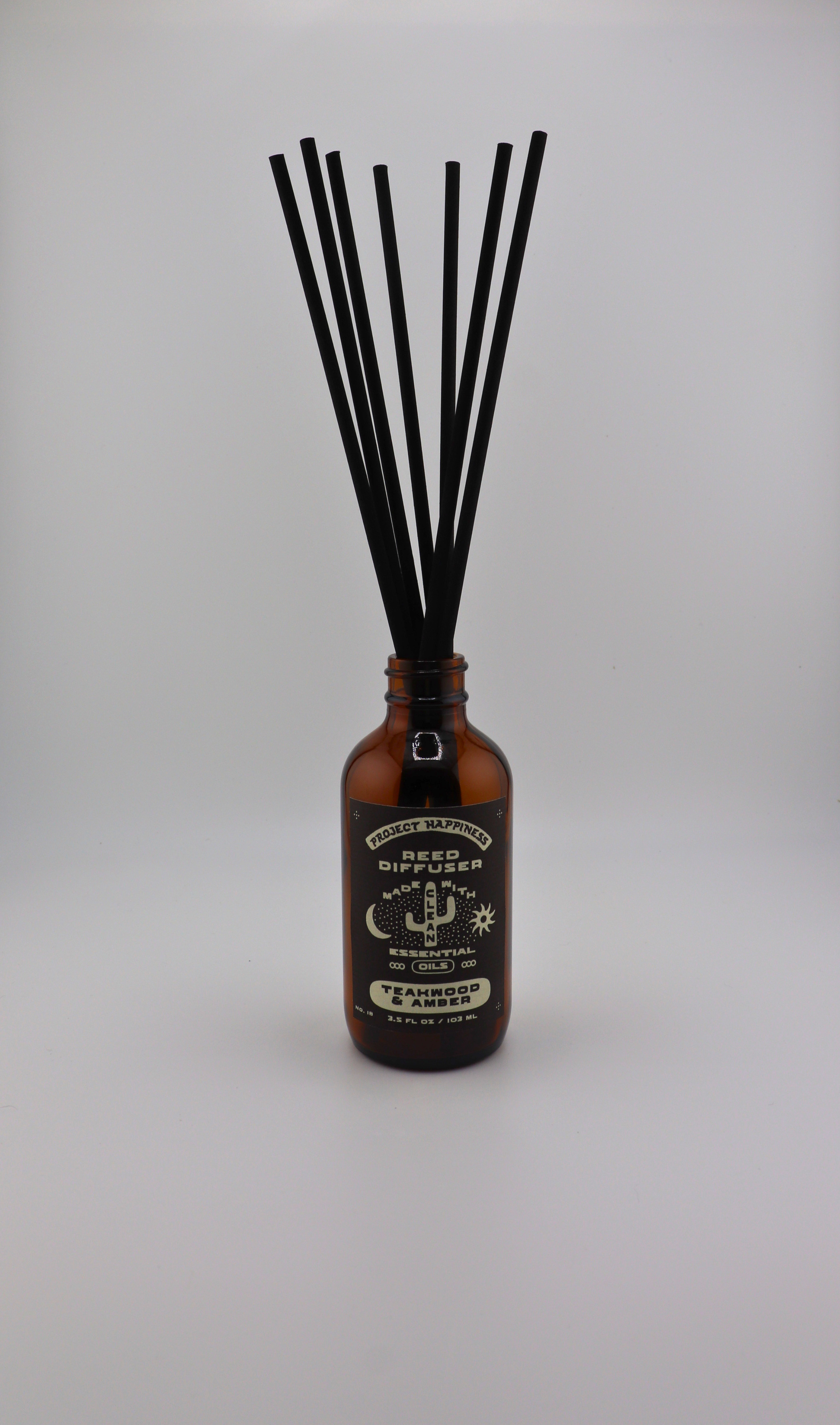 Teakwood & Amber Reed Diffuser in an amber glass bottle with 7 black reeds, featuring warm notes of teakwood, sandalwood, leather, amber, cedar, and dark musk. Lasts 3–4 months.