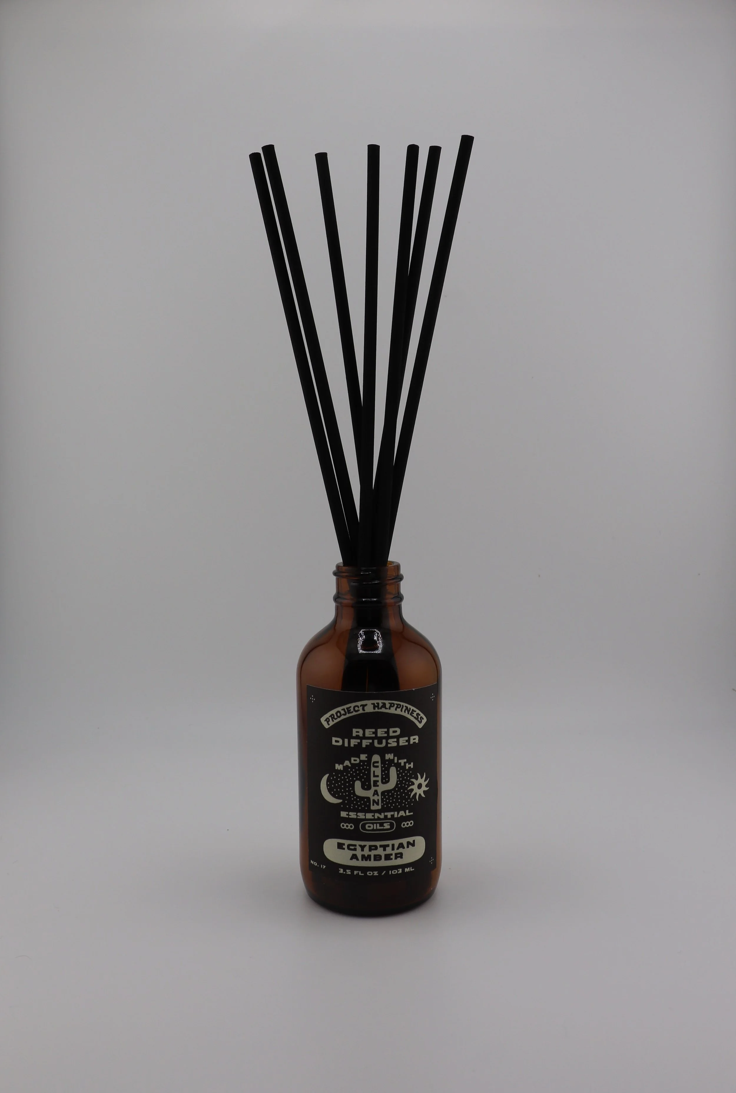 Egyptian Amber Reed Diffuser in an amber glass bottle with 7 black reeds, featuring warm notes of amber, sandalwood, patchouli, jasmine, musk, and tonka bean. Lasts 3–4 months.