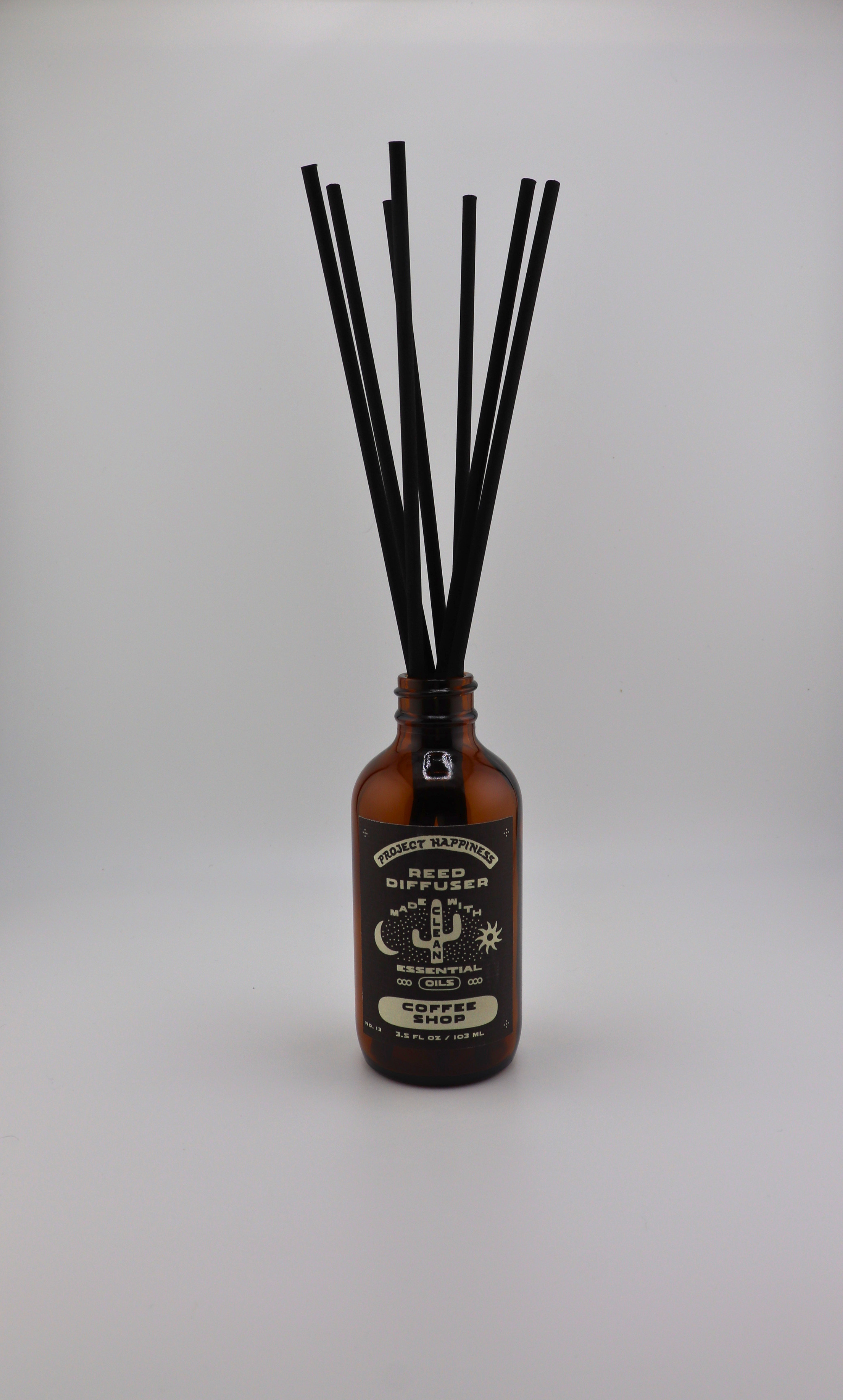 Coffee Shop Reed Diffuser in an amber glass bottle with 7 black reeds, featuring cozy notes of coffee, caramel, sugar, vanilla, and creamy milk. Lasts 3–4 months.