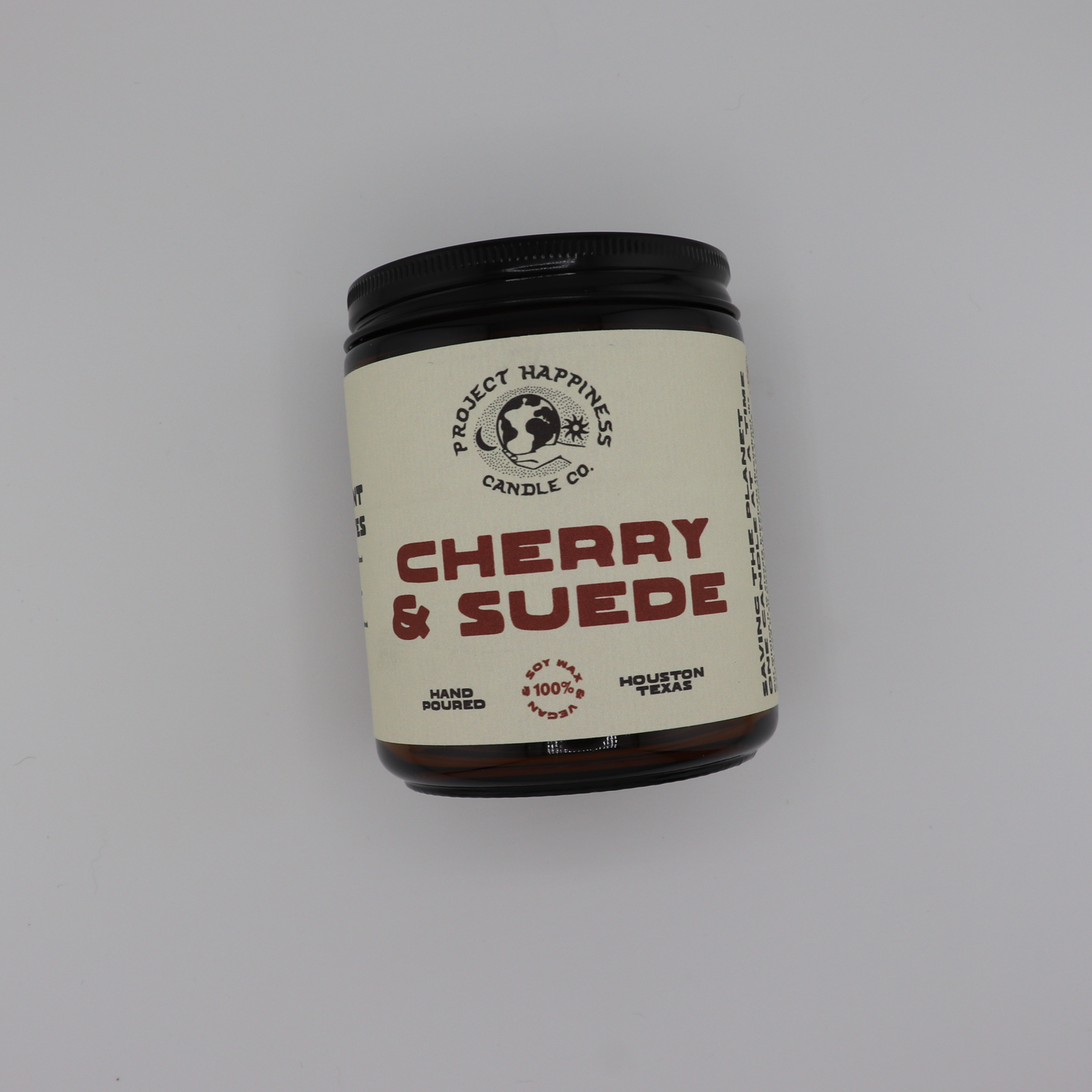 Cherry & Suede soy candle in an amber glass jar, featuring rich notes of black cherry, saffron, vanilla, incense, leather, amber, and sandalwood. Burns for 45–50 hours.