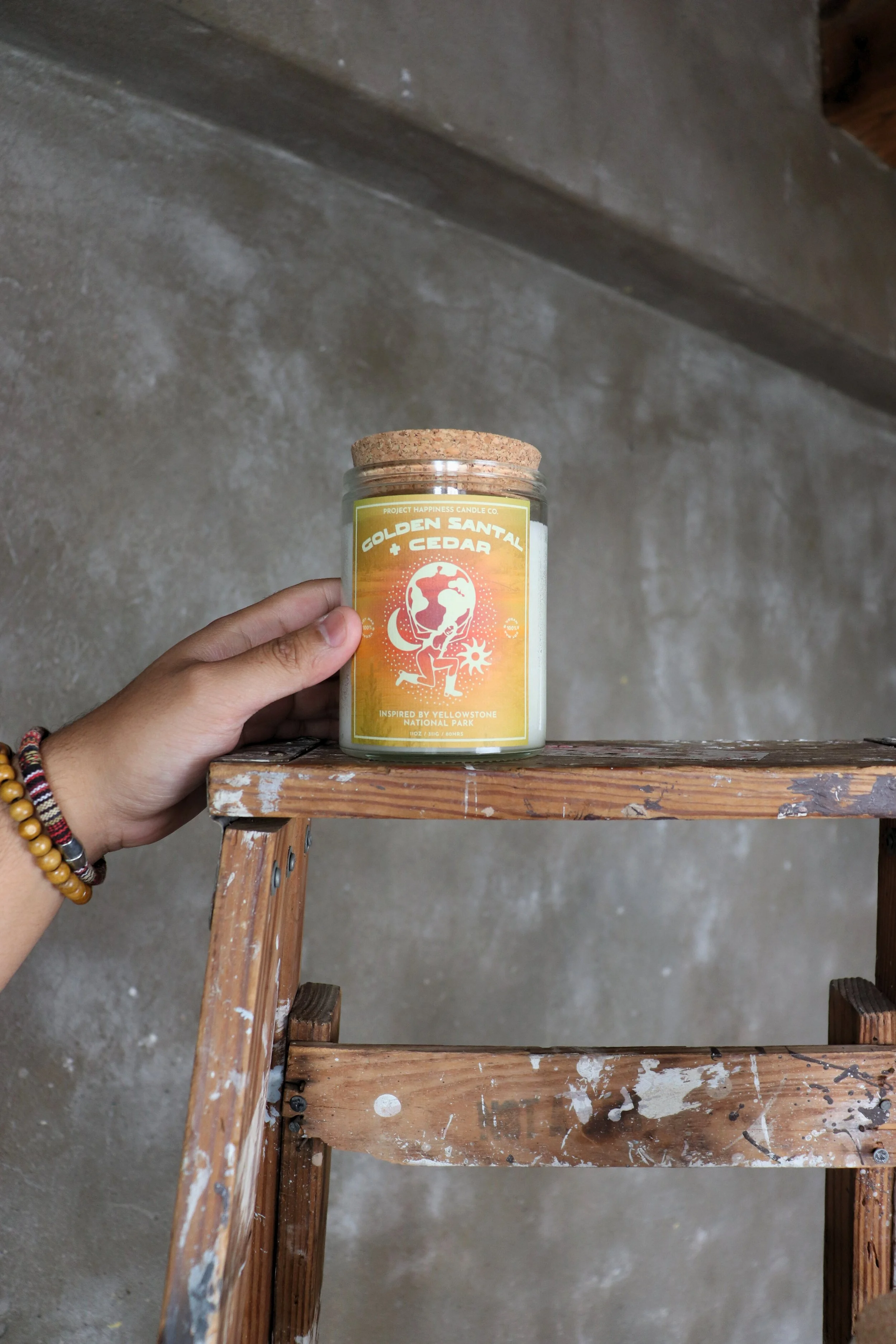 A hand grips a jar of "Golden Santal and Cedar Soy Candle," emphasizing its stylish label and warm, aromatic appeal.
