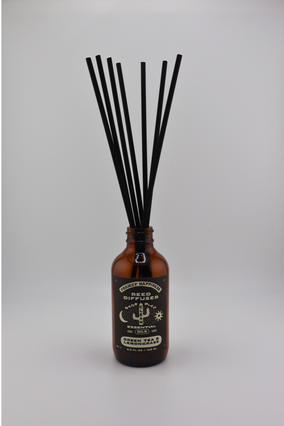 Green Tea & Lemongrass Reed Diffuser in an amber glass bottle with 7 black reeds, featuring fresh notes of lemongrass, green tea, jasmine, citrus, and light musk. Lasts 3–4 months.