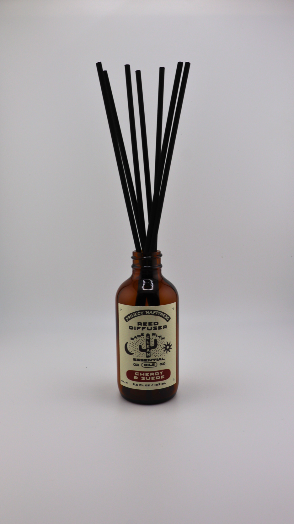 Cherry & Suede Reed Diffuser in an amber glass bottle with 7 black reeds, featuring rich notes of black cherry, vanilla, leather, amber, sandalwood, and incense. Lasts 3–4 months.