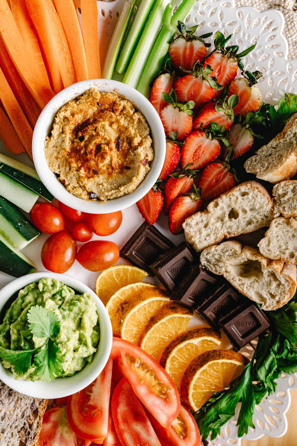 Overhead shot of an appetizer platter for sharing with guacamole, hummus, bread, crudités, chocolate, and strawberries