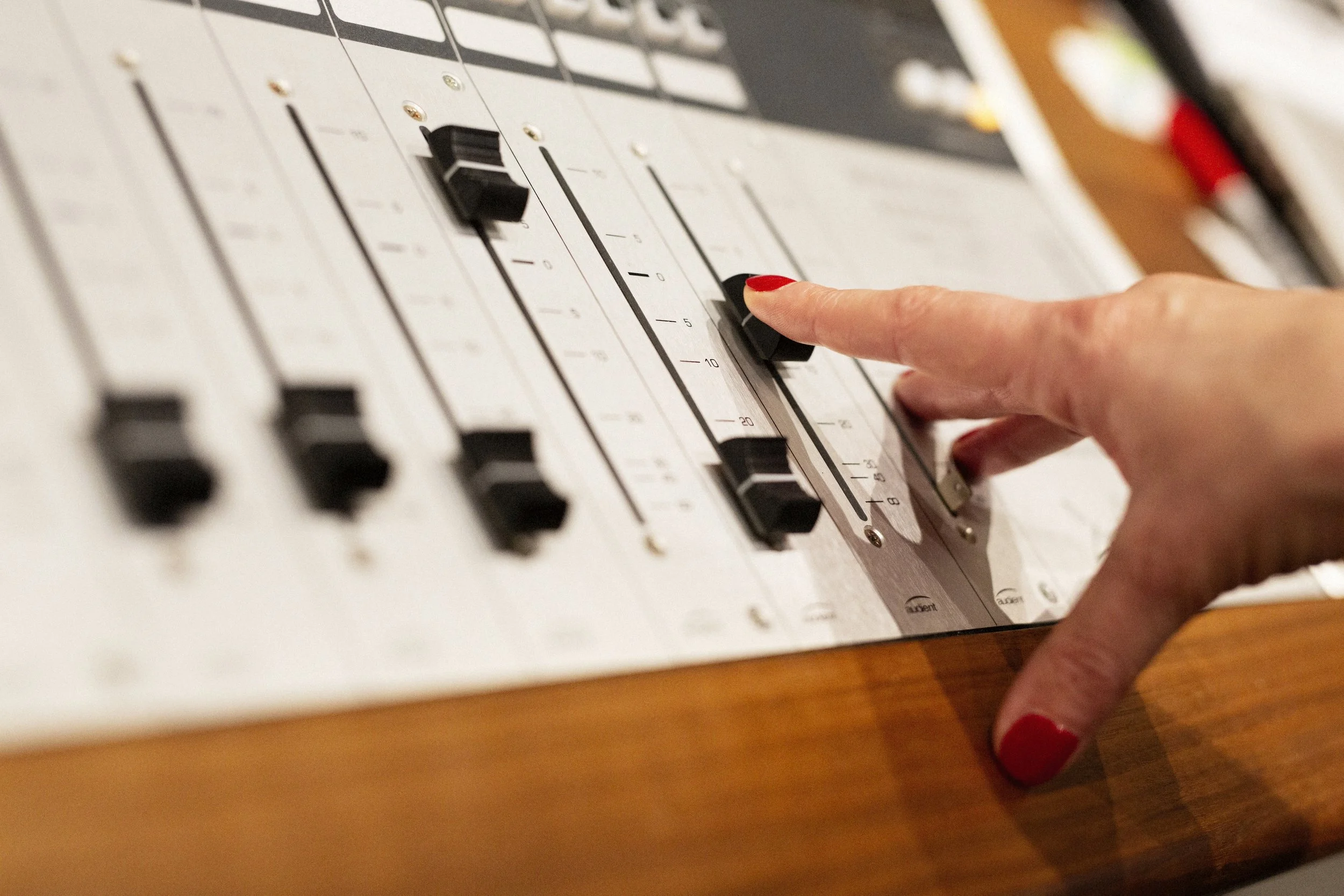 Close-up of a person's hand with red nail polish adjusting a control knob on an audio mixer or control panel.