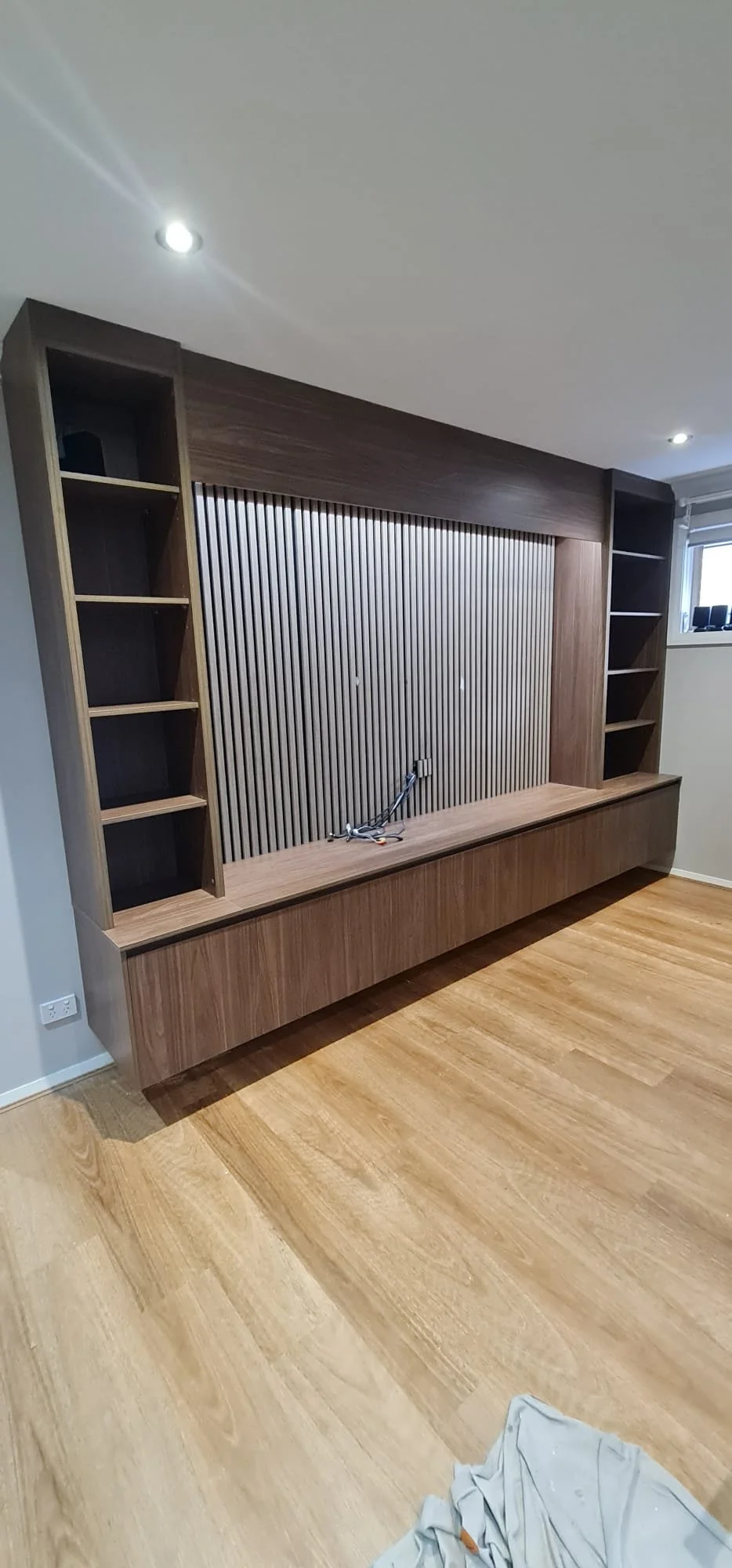 Walnut-toned media wall with vertical slatted panel behind the television, tall columns each end