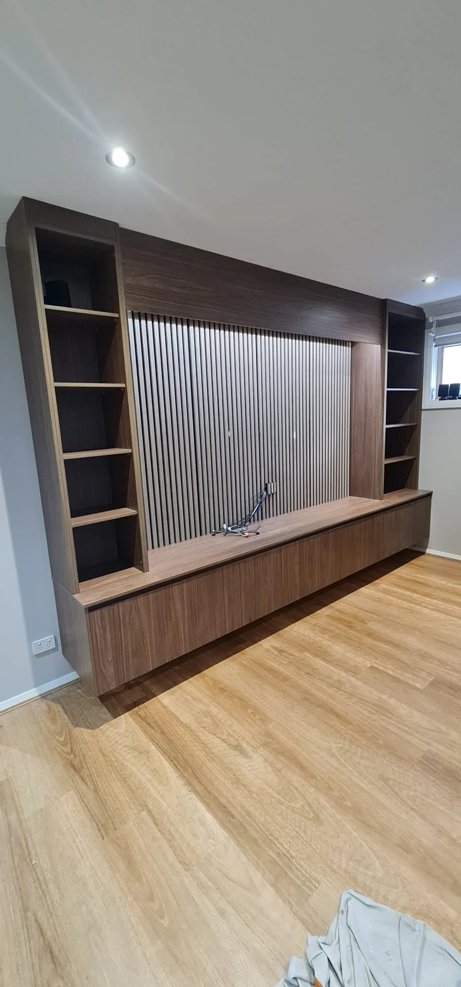 Angled view of the walnut media wall showing the depth of the slatted panel and floating base cabinet
