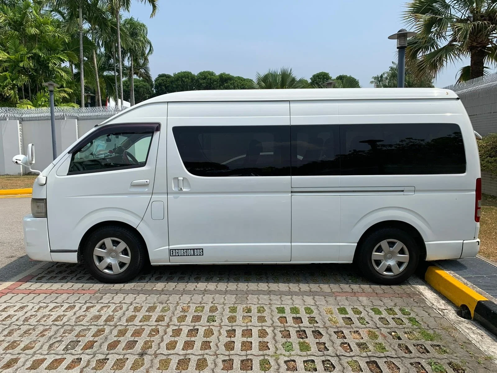 White passenger bus parked in a lot with trees and other buses in the background.
